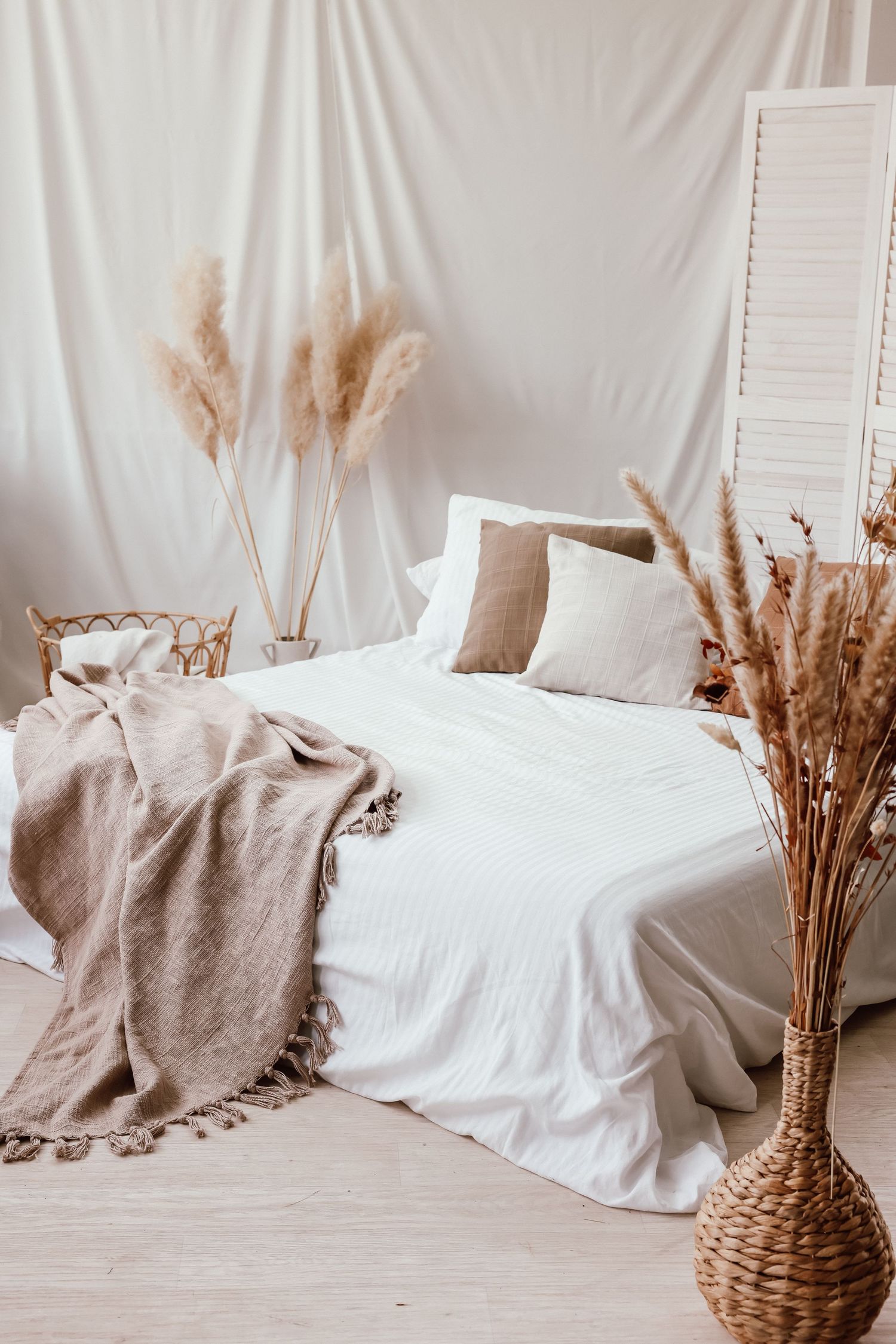 Boho bedroom with white bedding, taupe throw blanket, pampas grass decor, wicker vase, and neutral tones.