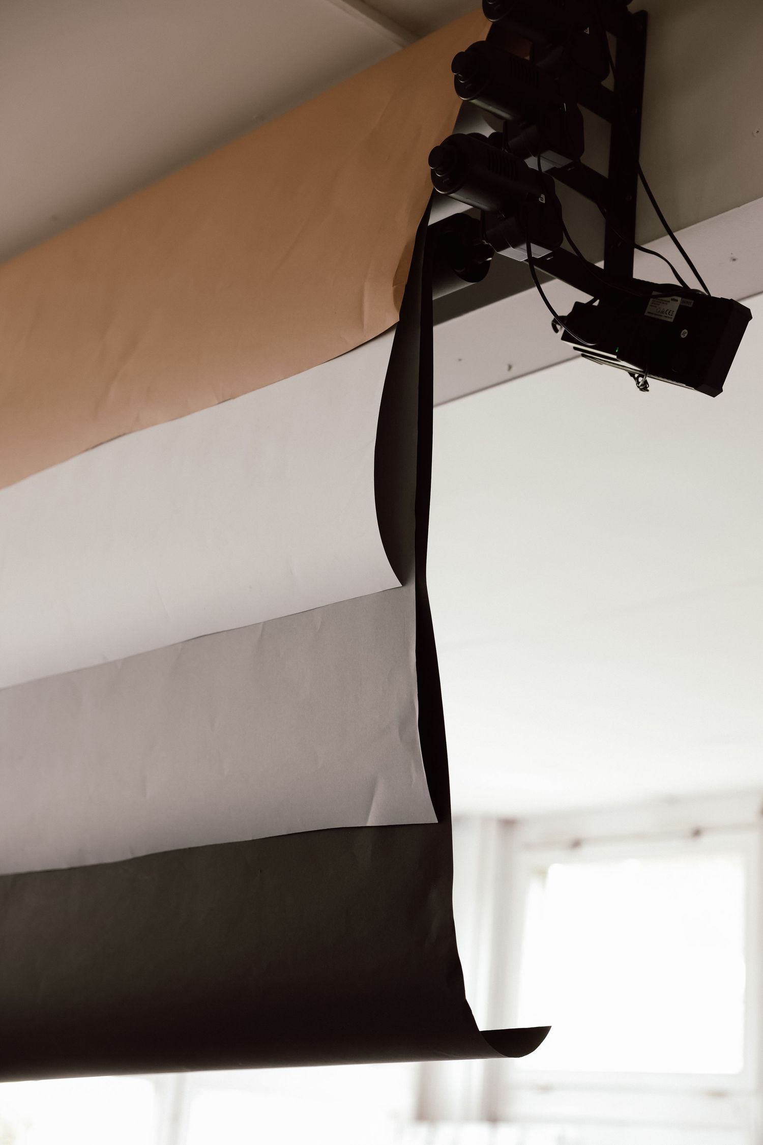 Rolled backdrop paper in black, white, and tan hanging from ceiling mount in a photography studio.