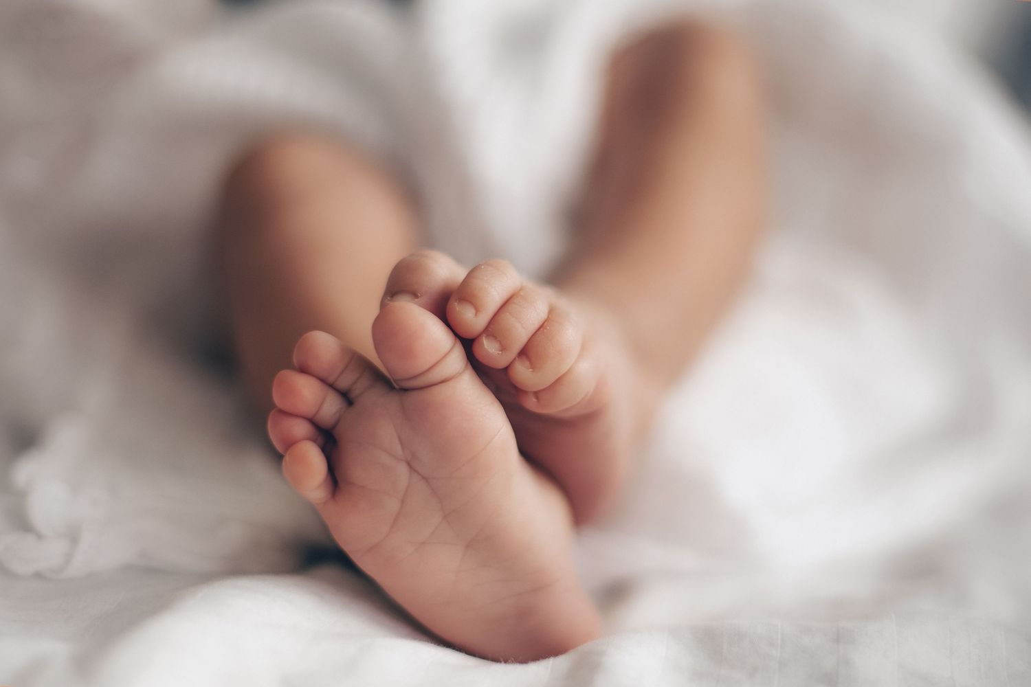 Close-up of tiny newborn baby feet resting on a soft white blanket, perfect for birth announcements.