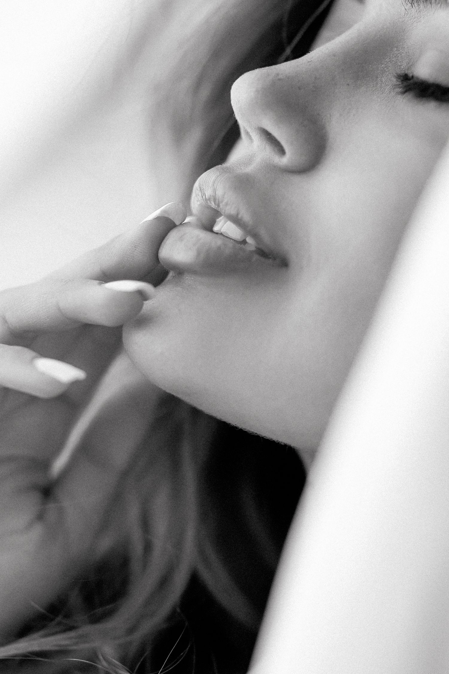 Black and white close-up portrait of a woman touching her lips with her finger, showcasing natural beauty.