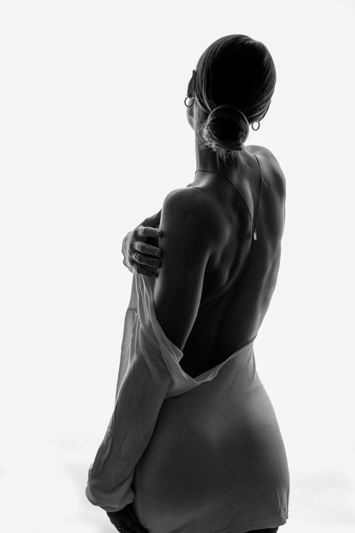 Black and white photo of a woman in a backless dress, viewed from behind, with elegant posture and hair up.