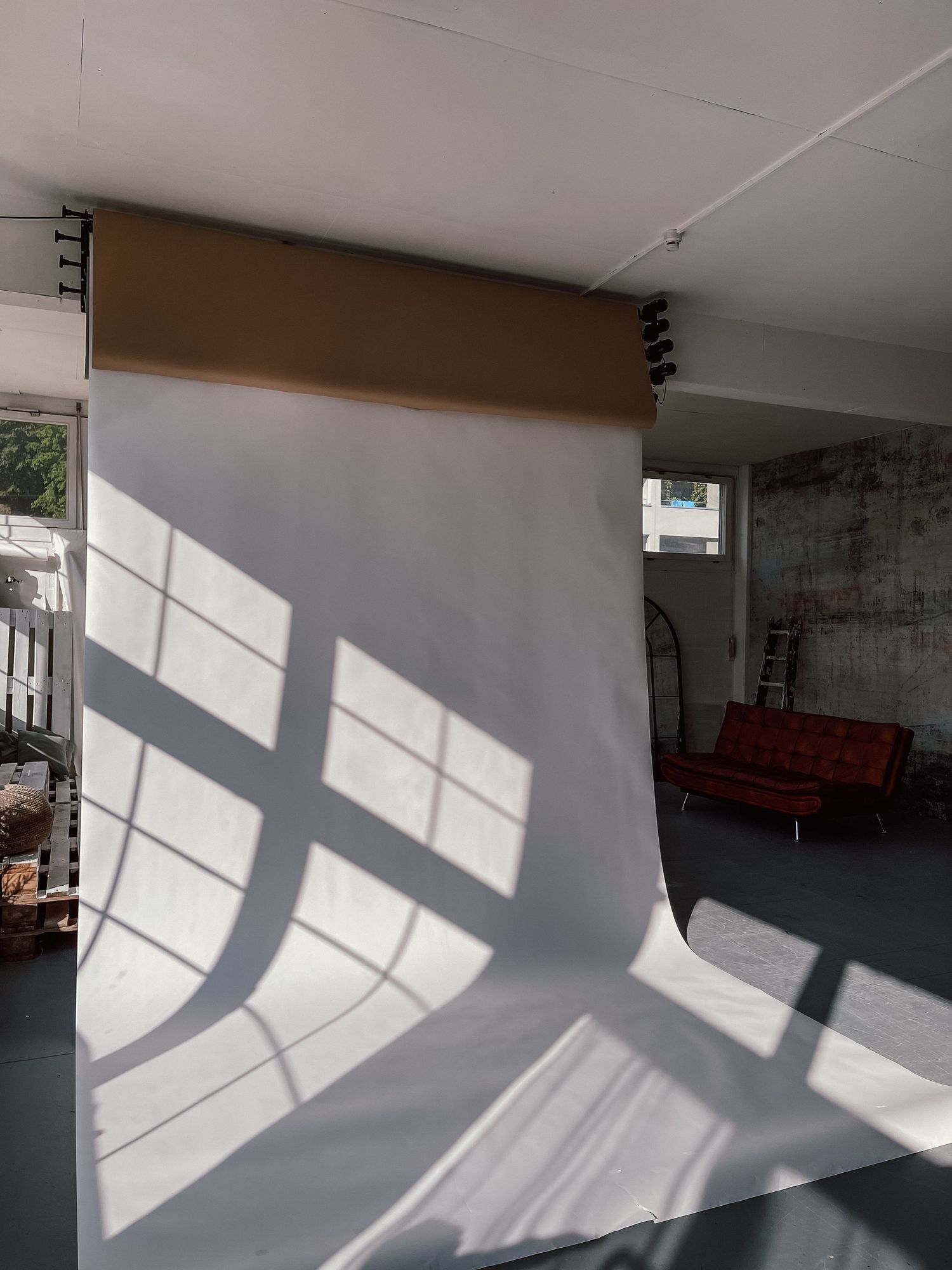 Large white photography backdrop on a ceiling-mounted roll in a spacious studio with natural light and brick wall.