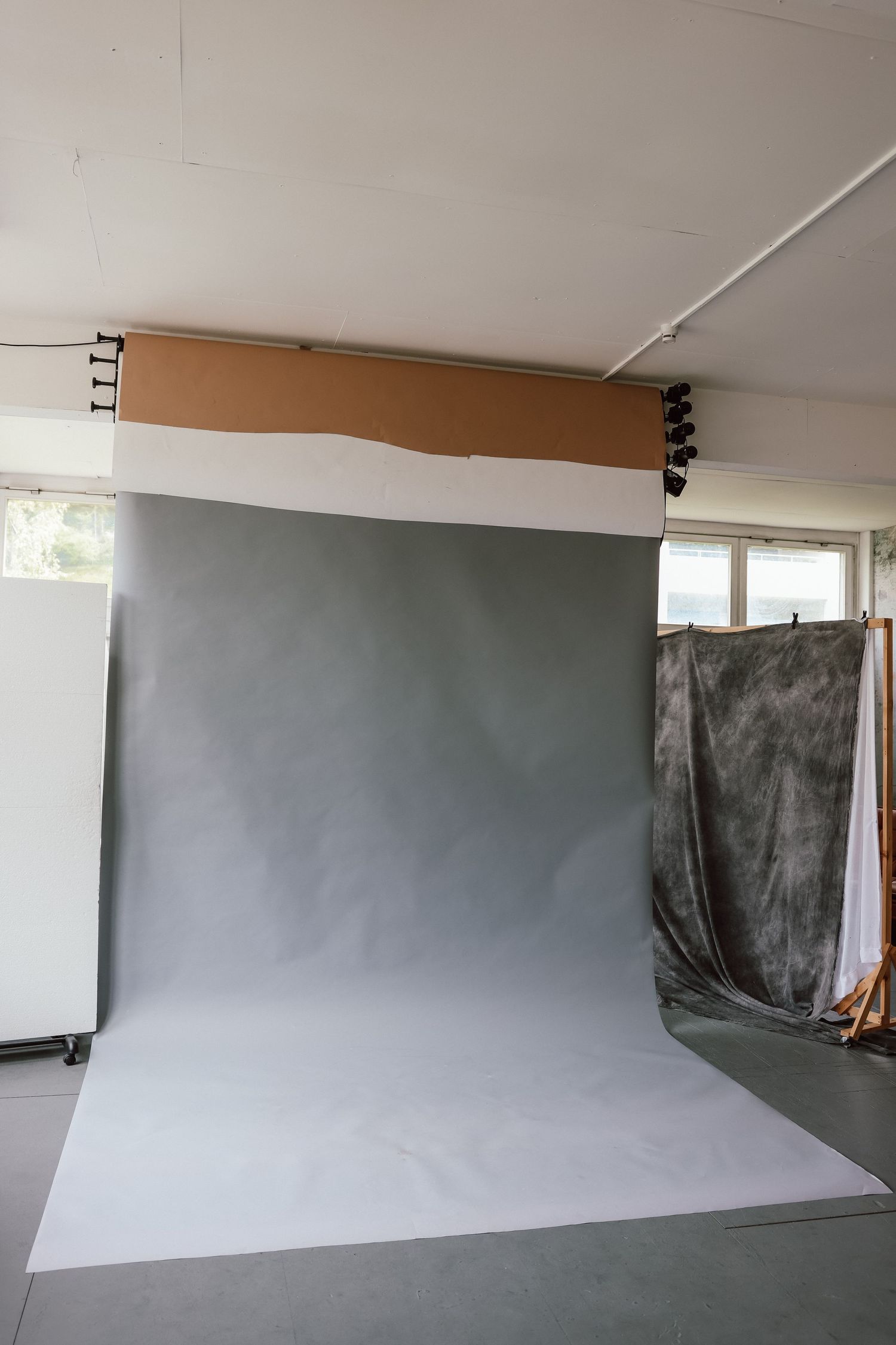 A professional photography studio with a large gray backdrop on a rolling stand with lighting equipment.