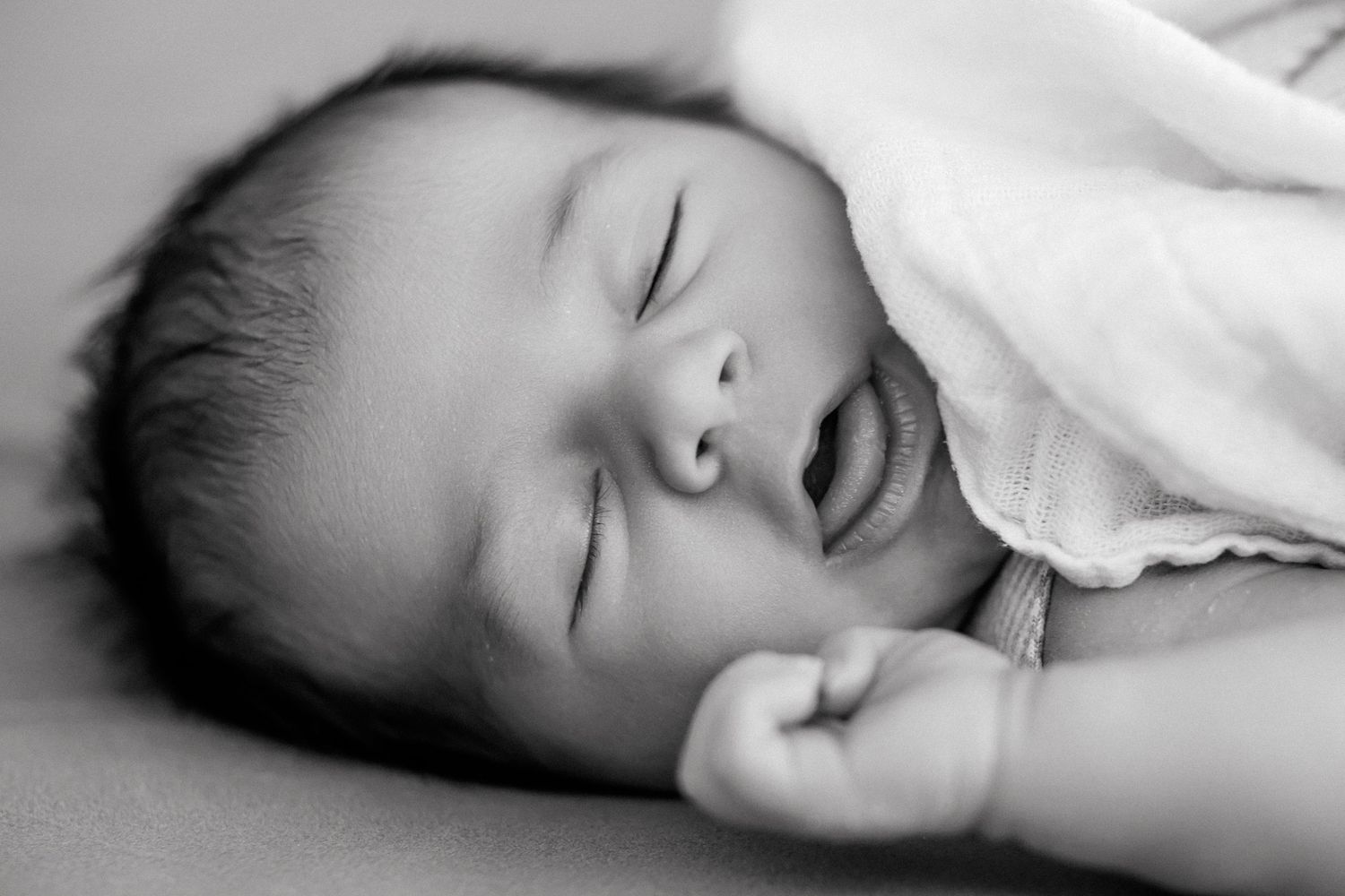 Peaceful newborn baby sleeping soundly, wrapped in white blanket, black and white portrait photography.