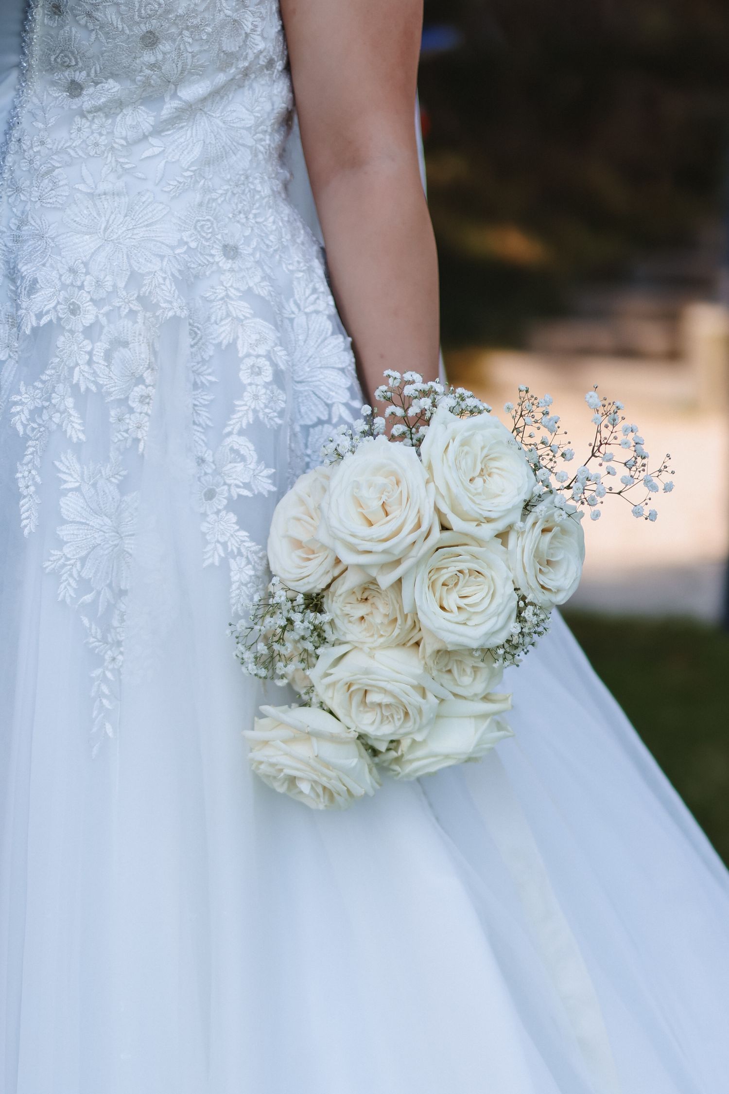 Bride in lace wedding gown holding elegant white rose bouquet with baby's breath accents.