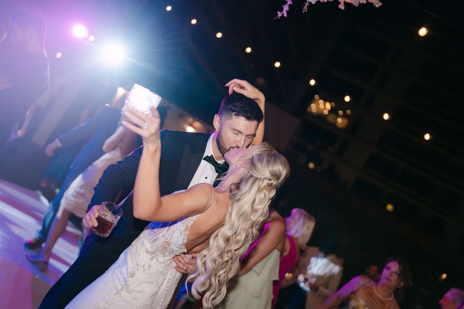 Bride and groom share a passionate first dance embrace under colorful lights at their wedding reception.