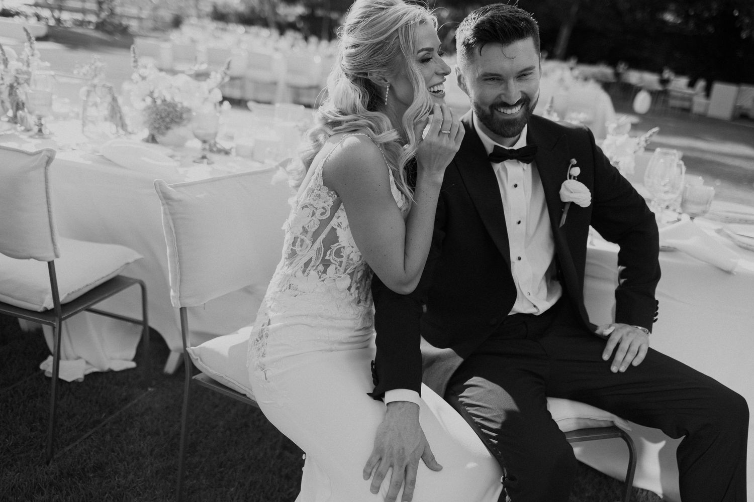 Bride and groom laughing joyfully together in black and white photo at outdoor wedding reception.