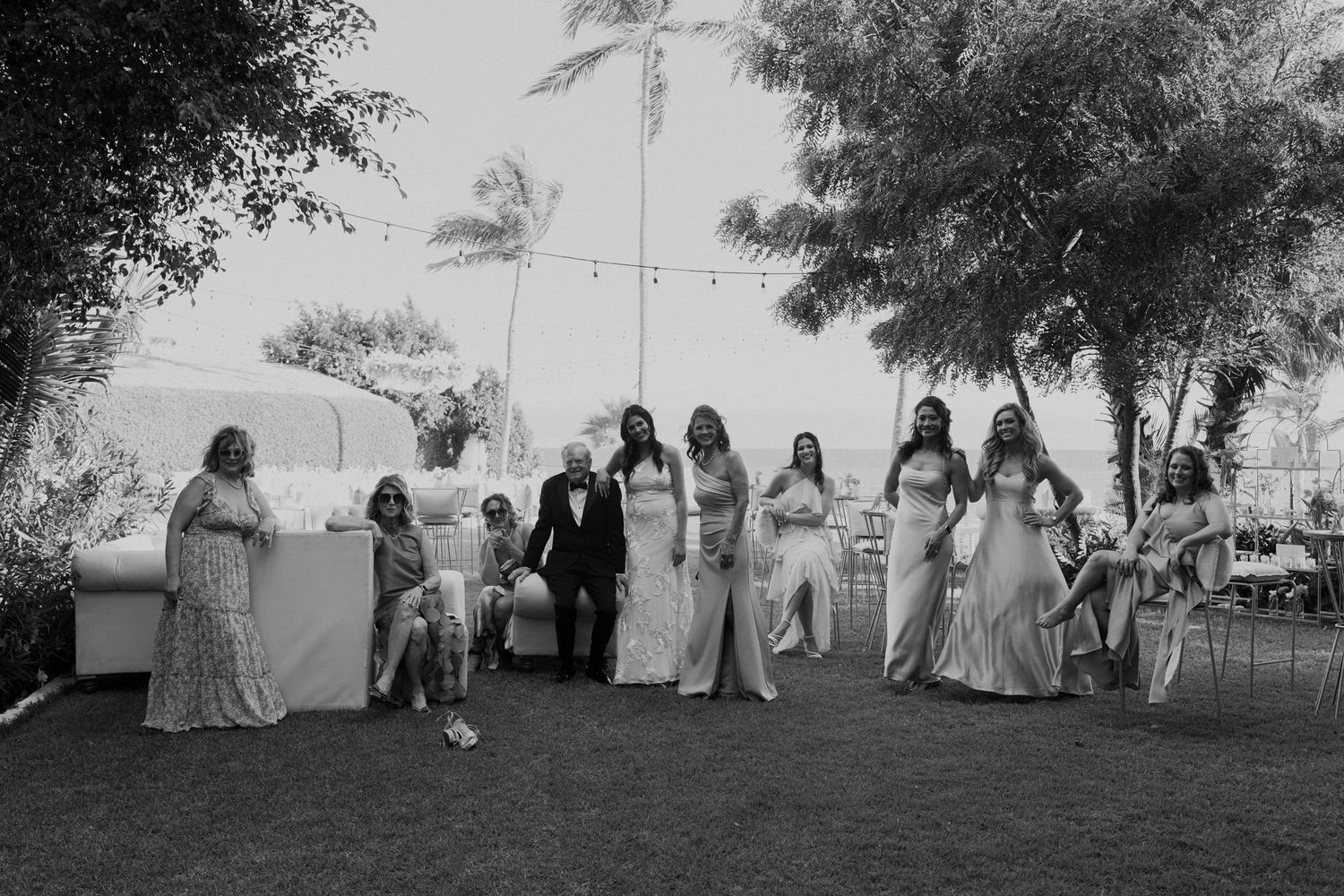 Black and white photo of bride, groom, and bridesmaids posing together in a tropical garden setting.