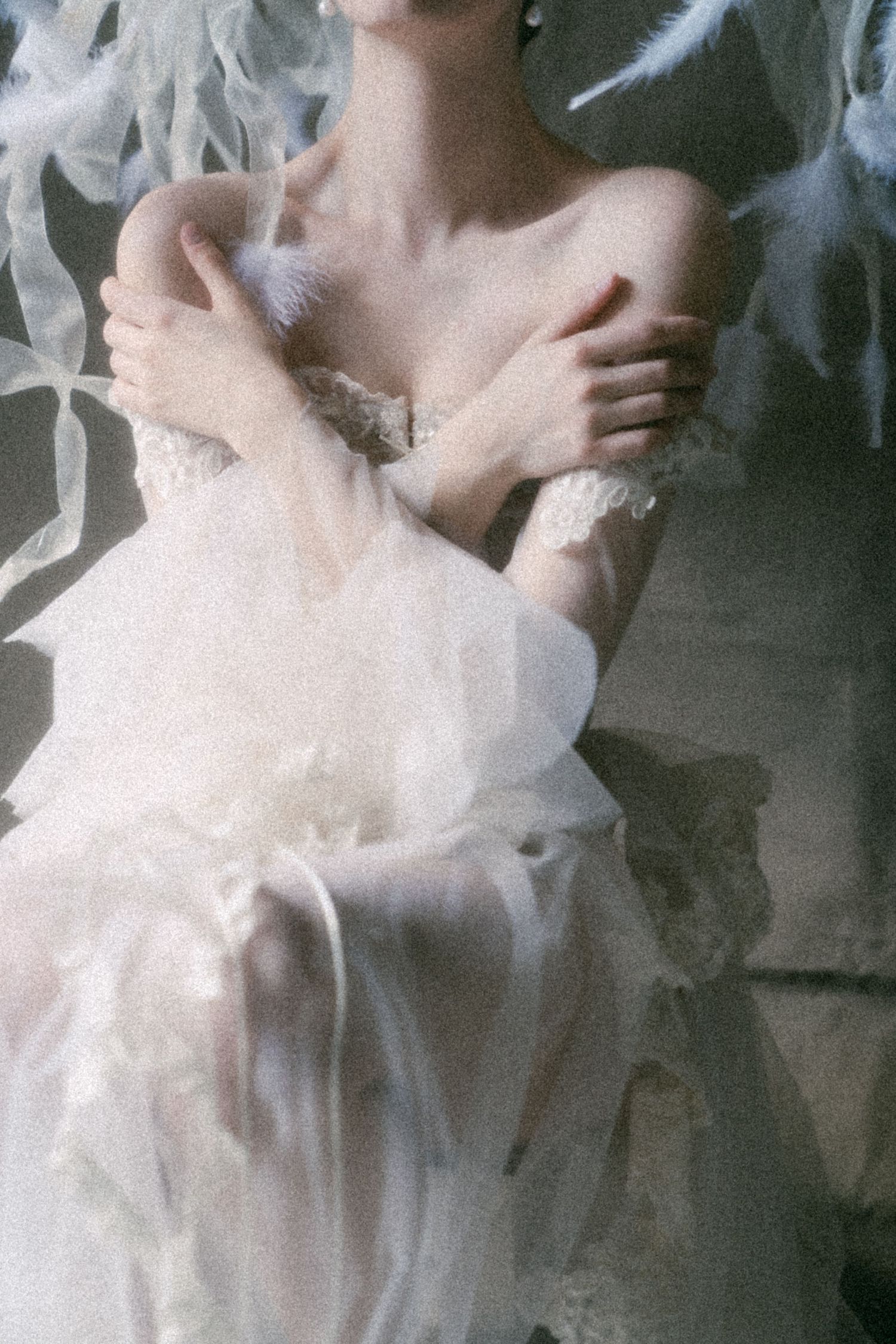 Ethereal bride in off-shoulder white tulle wedding gown surrounded by soft feathers in dreamy portrait.