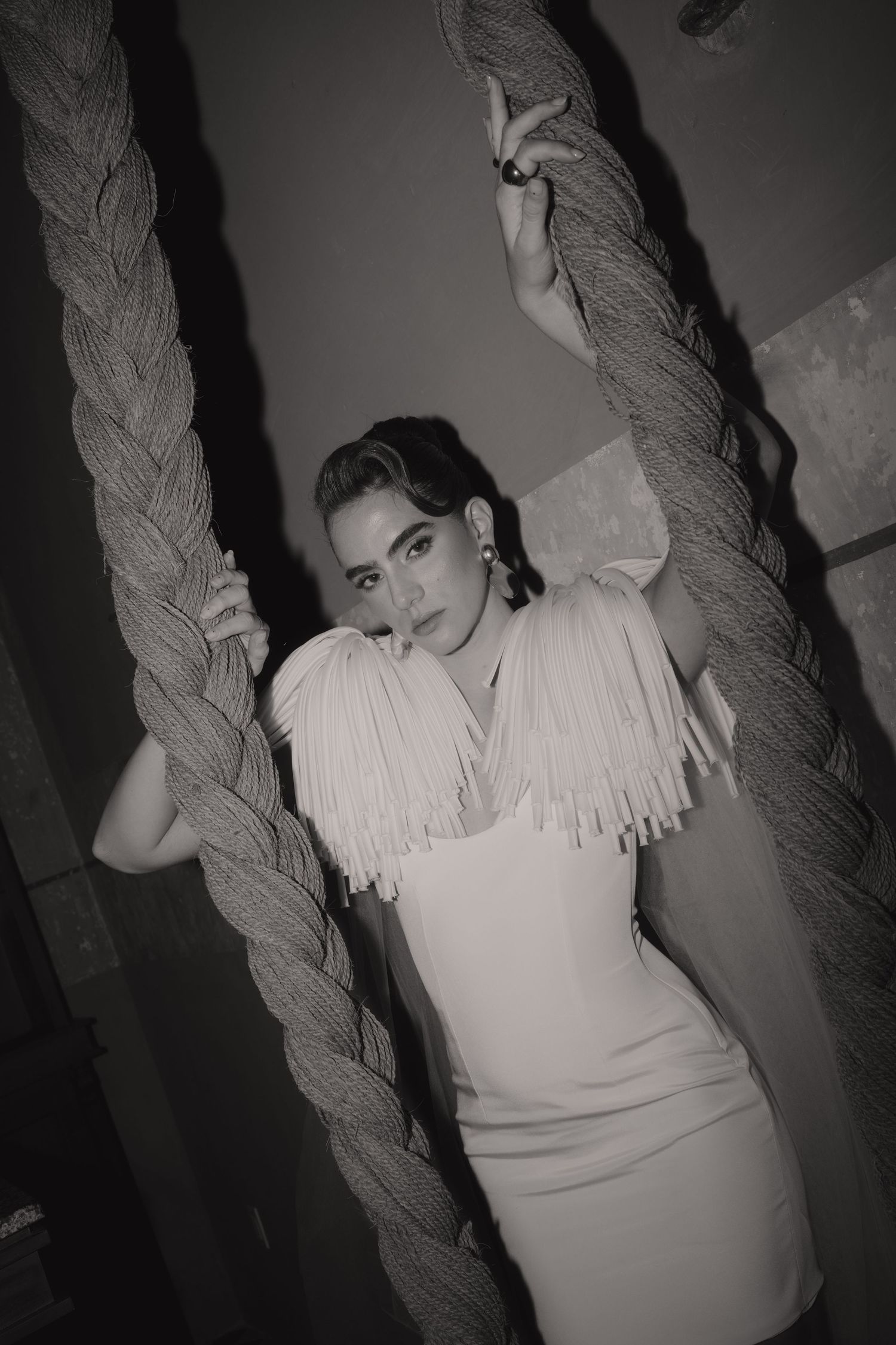 Black and white photo of bride in white dress posing between large decorative ropes dramatically.