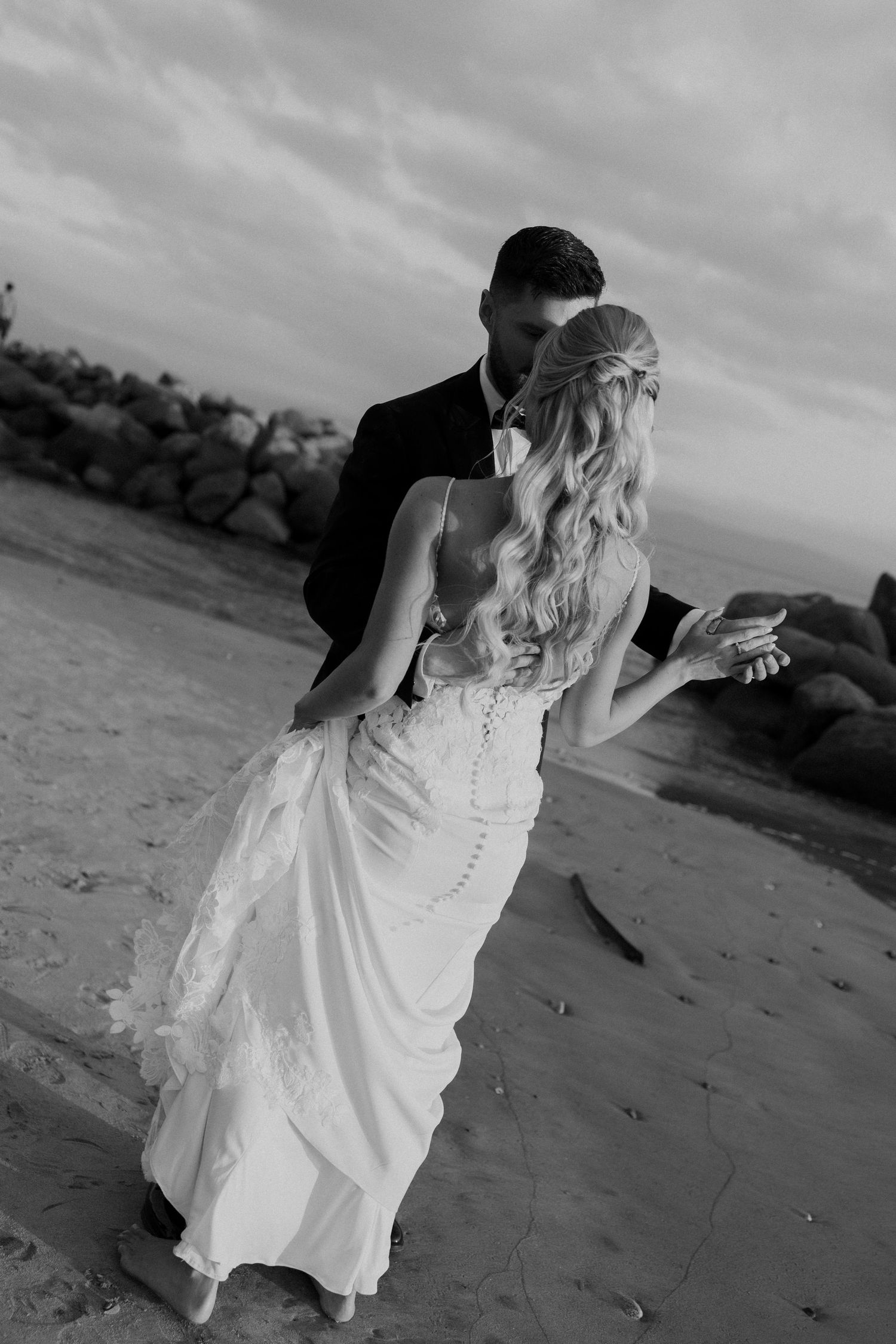 Black and white romantic wedding photo of bride and groom dancing together on a sandy beach.
