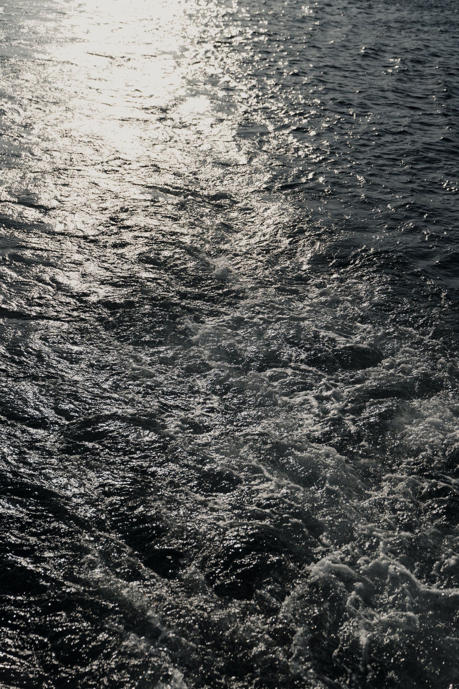 Sunlight reflecting on dark choppy ocean waves creating a dramatic silver and black water texture pattern.