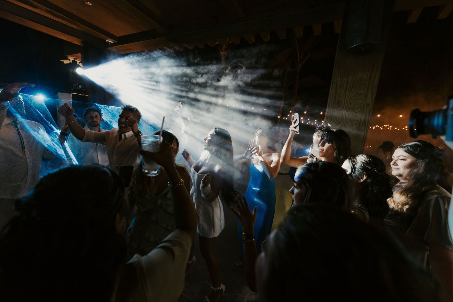 Dramatic wedding reception dance floor scene with guests celebrating under beams of blue light.