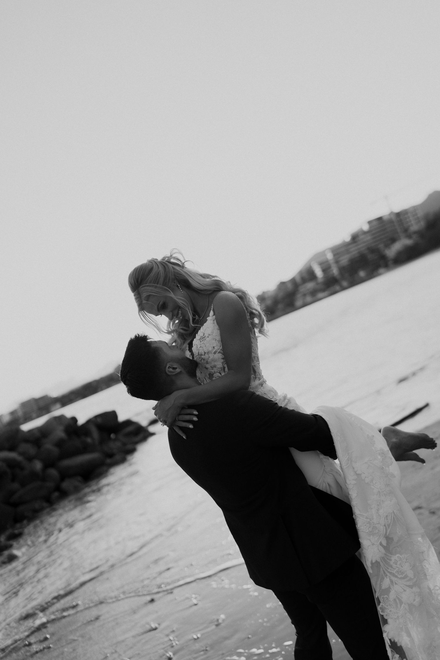Black and white photo of groom lifting bride for a kiss on the beach at their wedding.