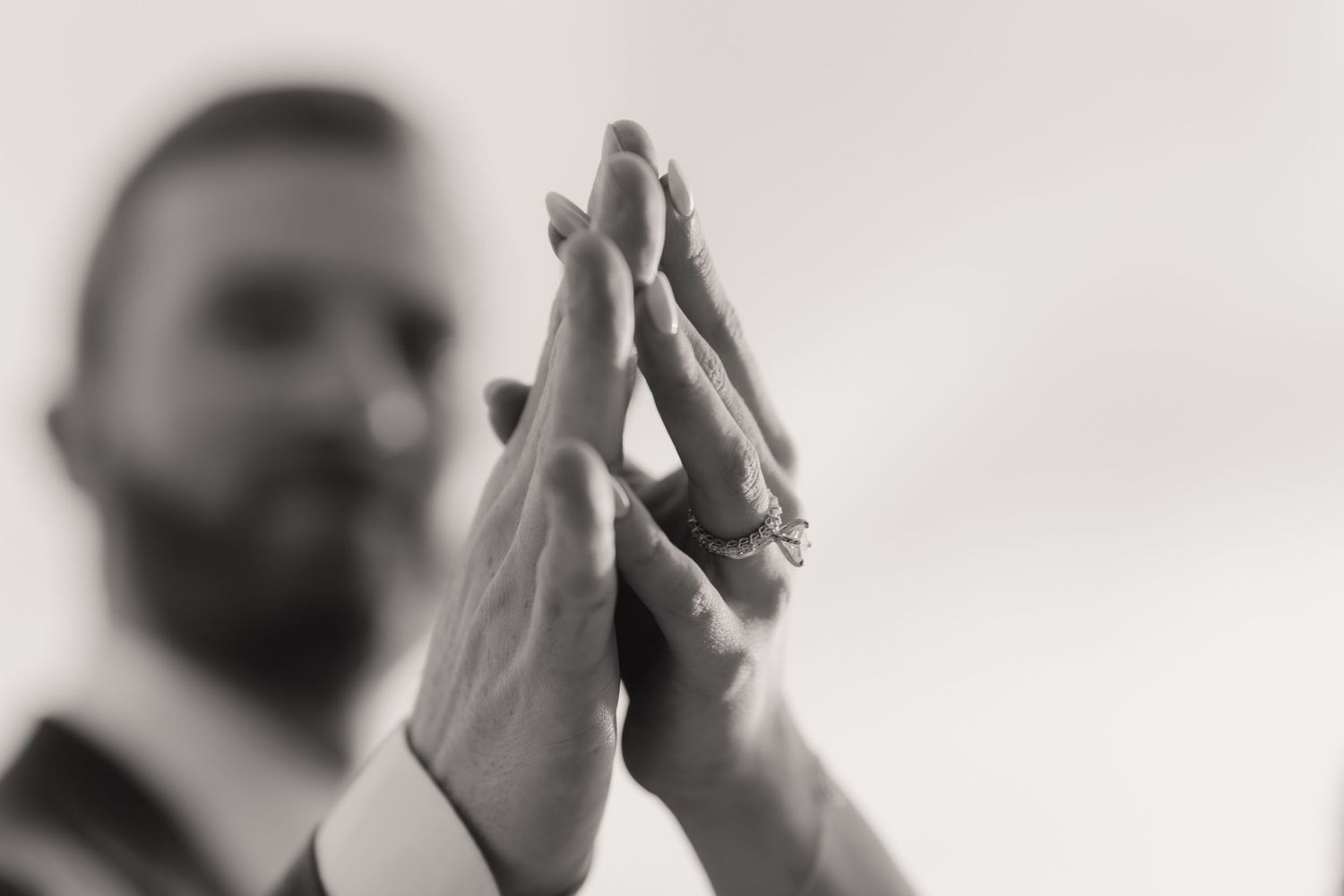 Bride and groom touching hands showing wedding ring in black and white close-up photo.