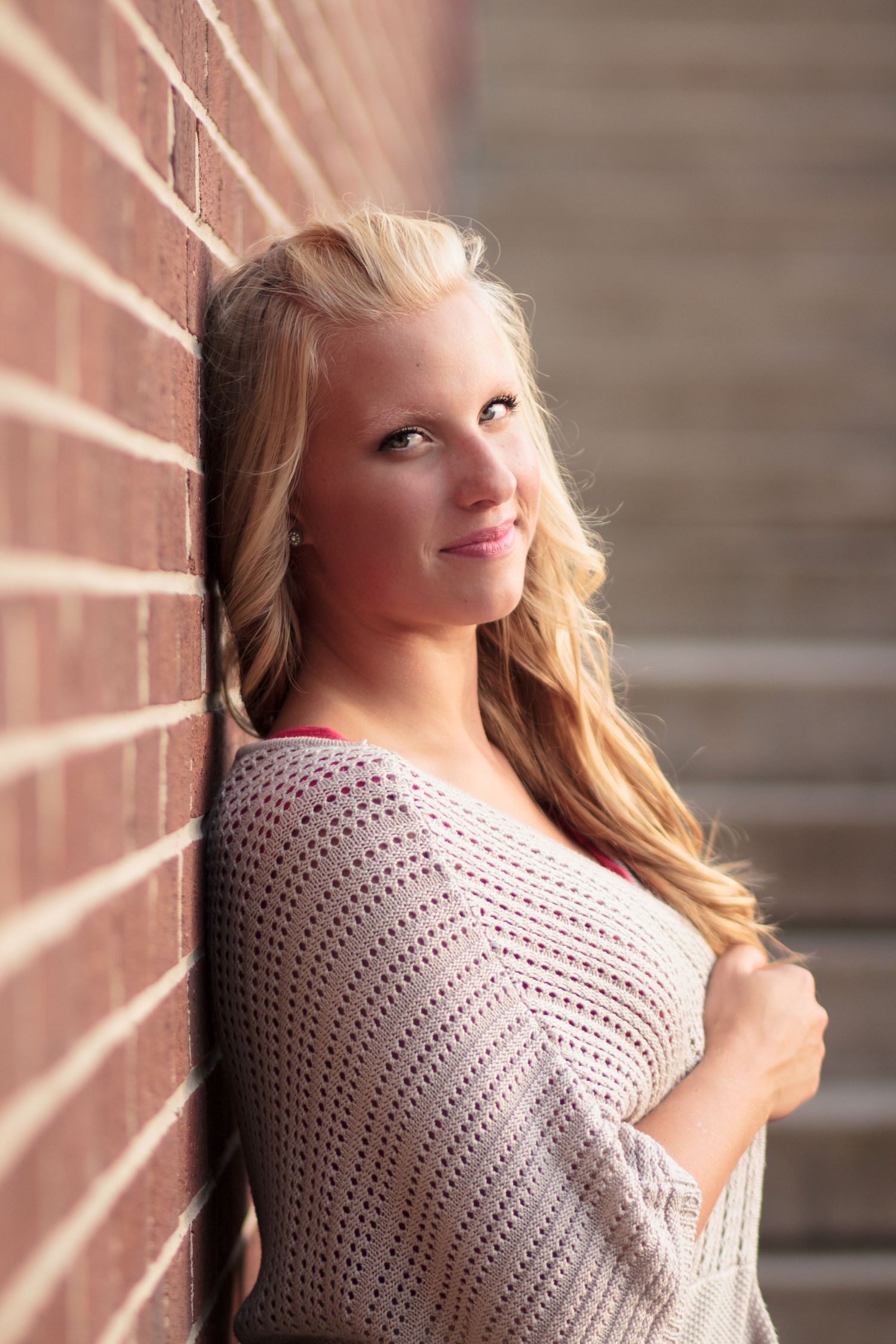 Portrait of someone in a pink sweater leaning against a brick wall in warm lighting.