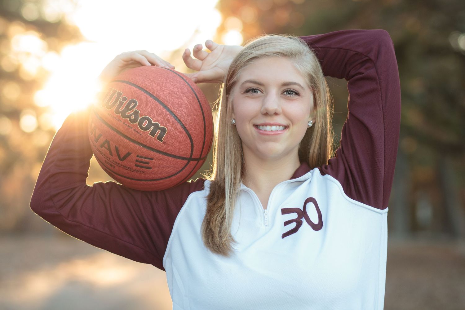 A player poses with basketball at sunset wearing white jersey.