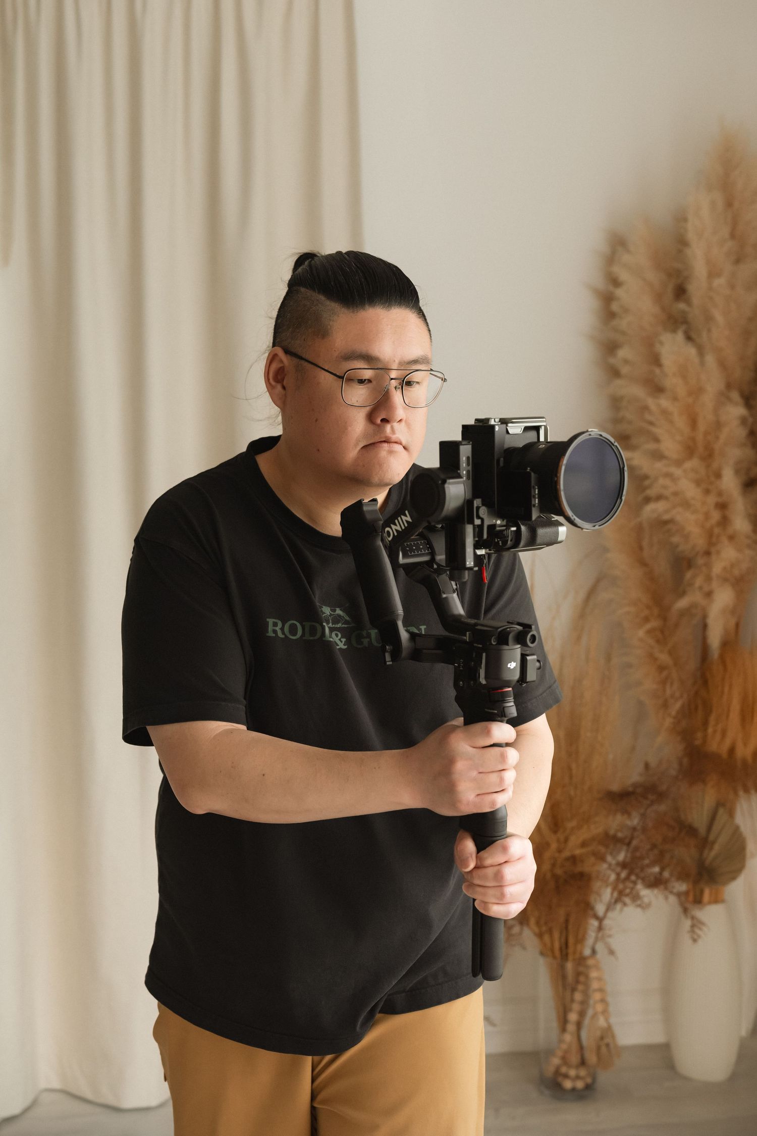 Videographer holding a camera gimbal stabilizer while reviewing footage in a studio setting.
