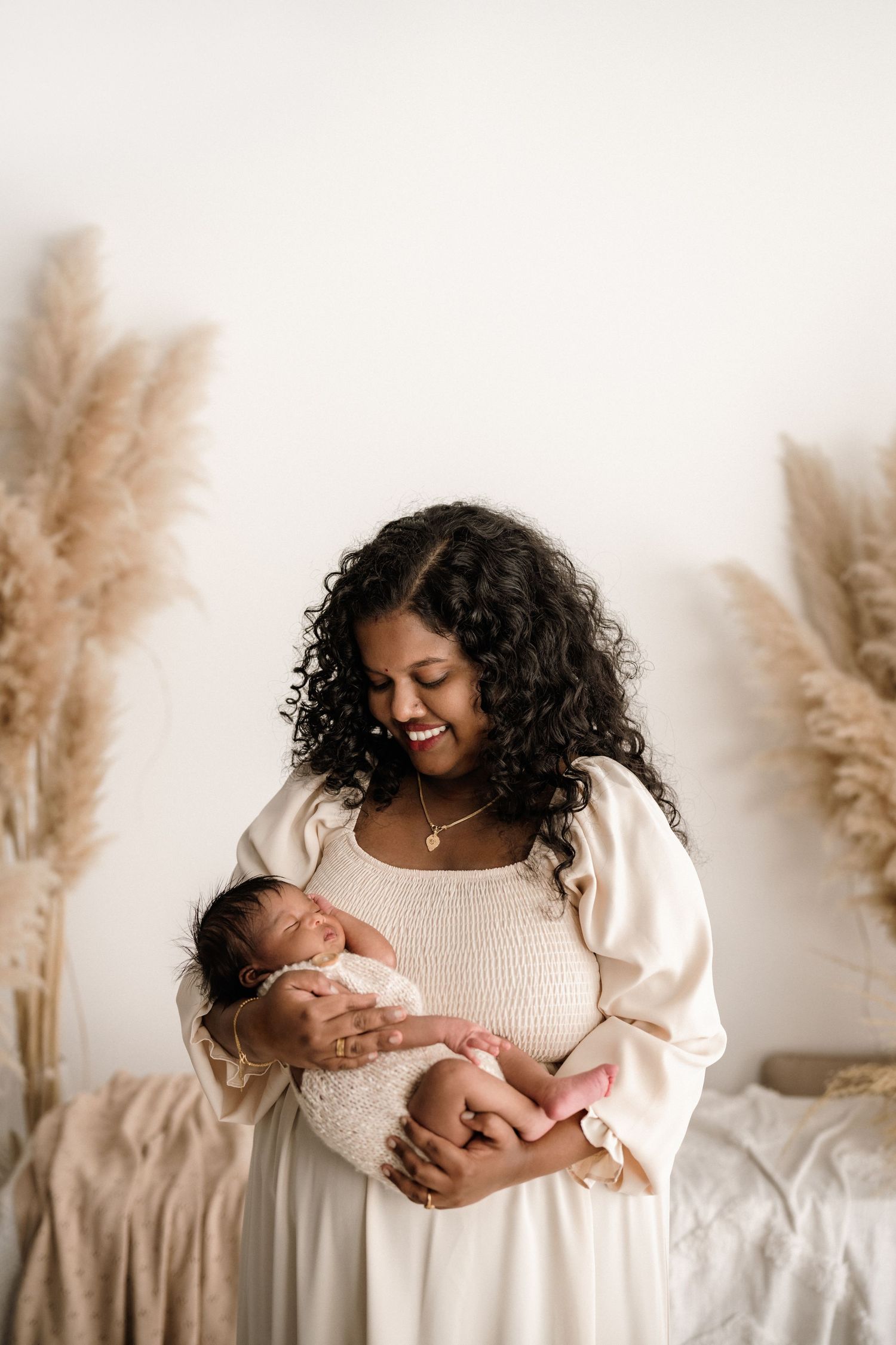 A tender moment captured with a newborn baby against a neutral backdrop with pampas grass decor in warm tones.
