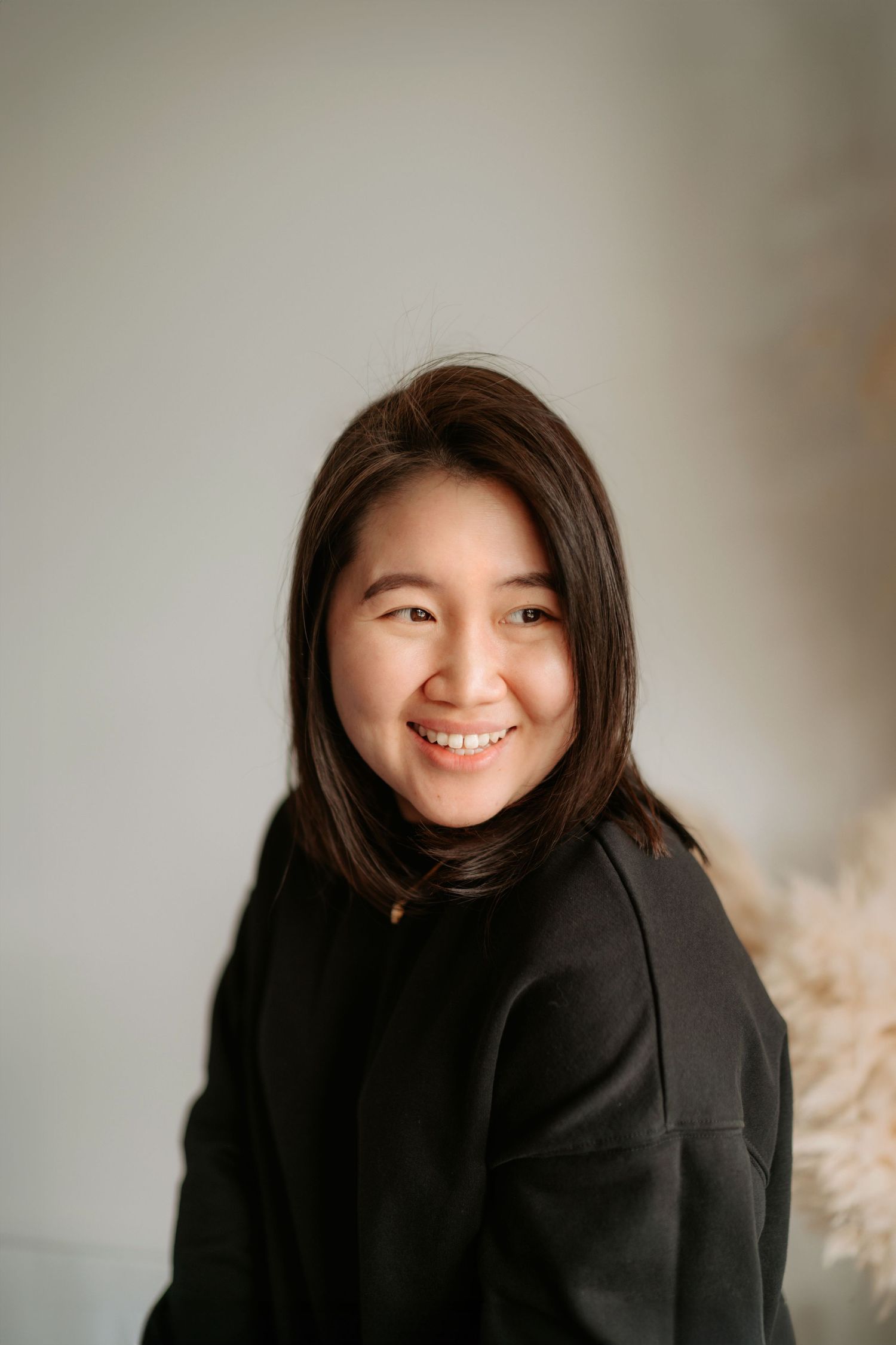 Candid portrait of woman in black sweater smiling warmly against neutral background.