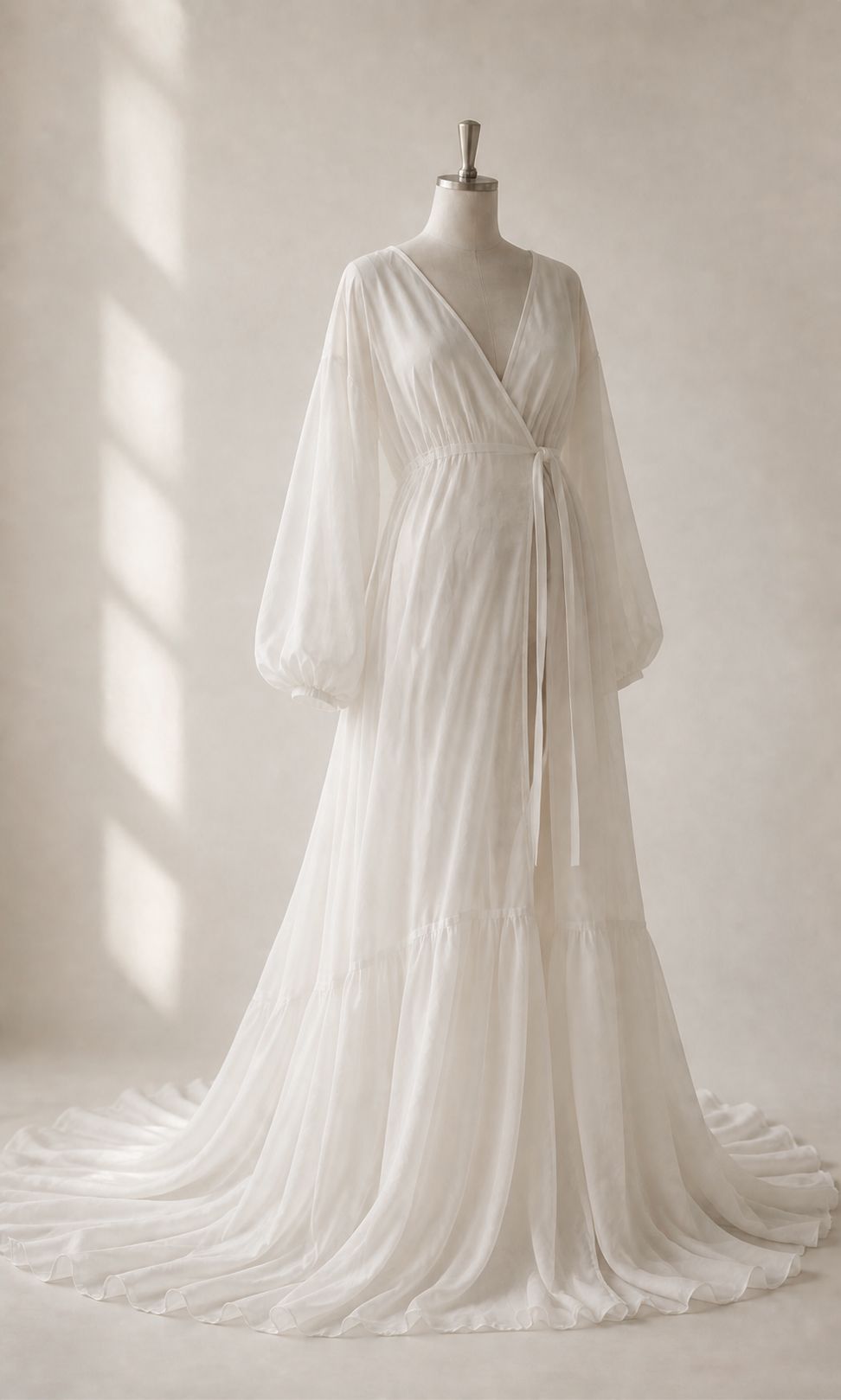 Elegant white chiffon wrap wedding gown with bishop sleeves, empire waist, and flowing tiered skirt on a dress form.