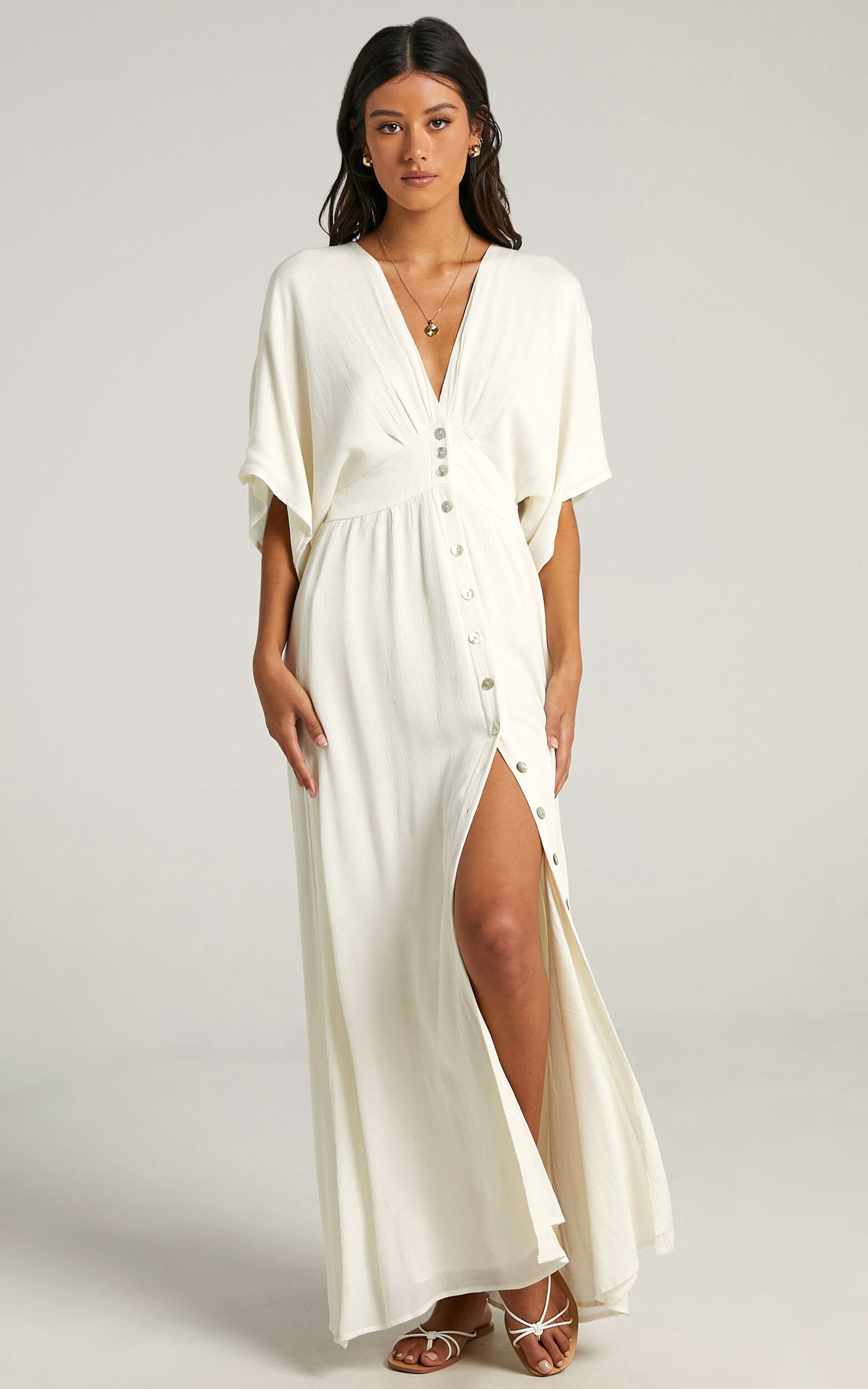 Elegant white maxi dress featuring kimono sleeves, button details, and high side slit worn with strappy sandals.