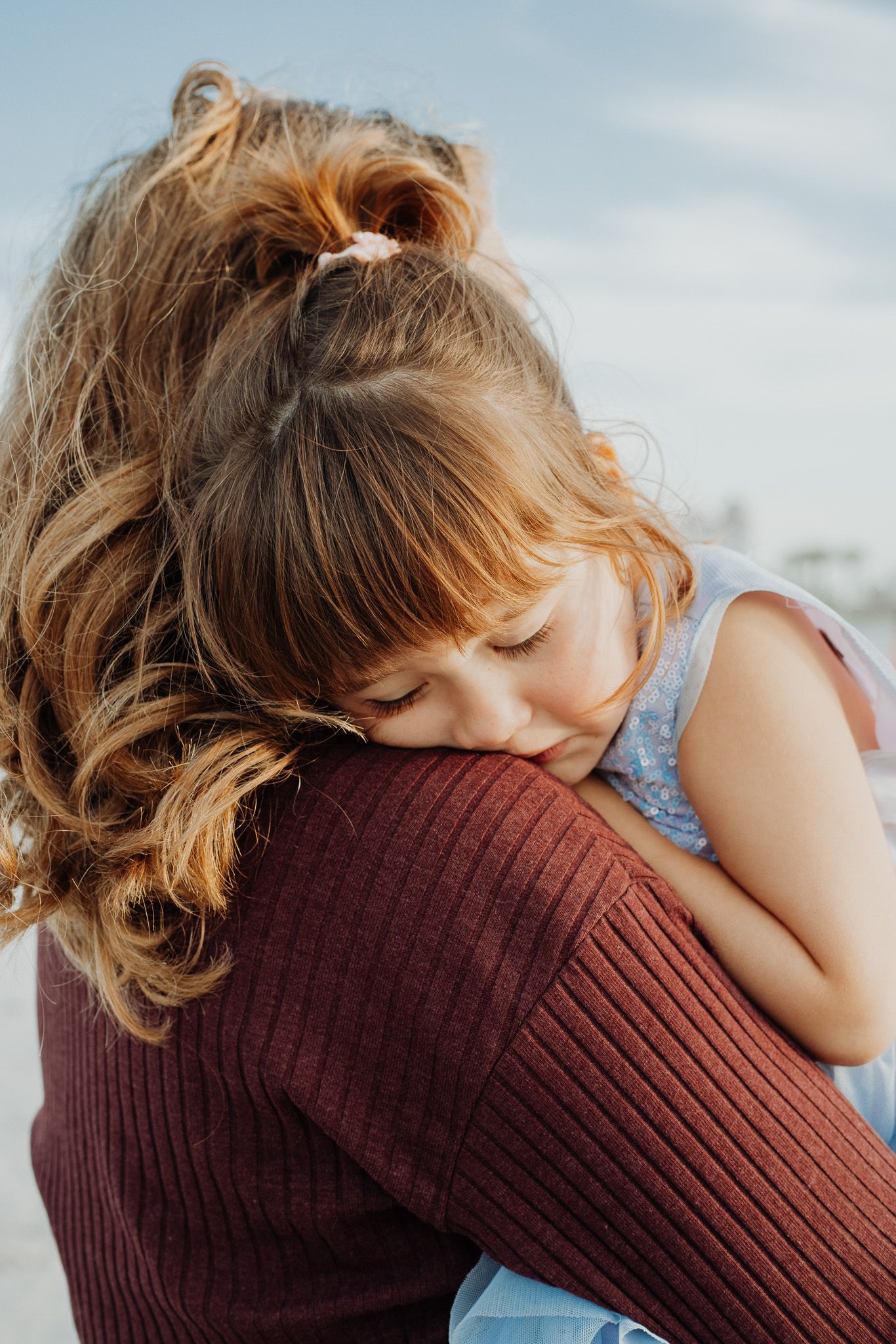 Child resting peacefully on someone's shoulder in a cozy maroon sweater.