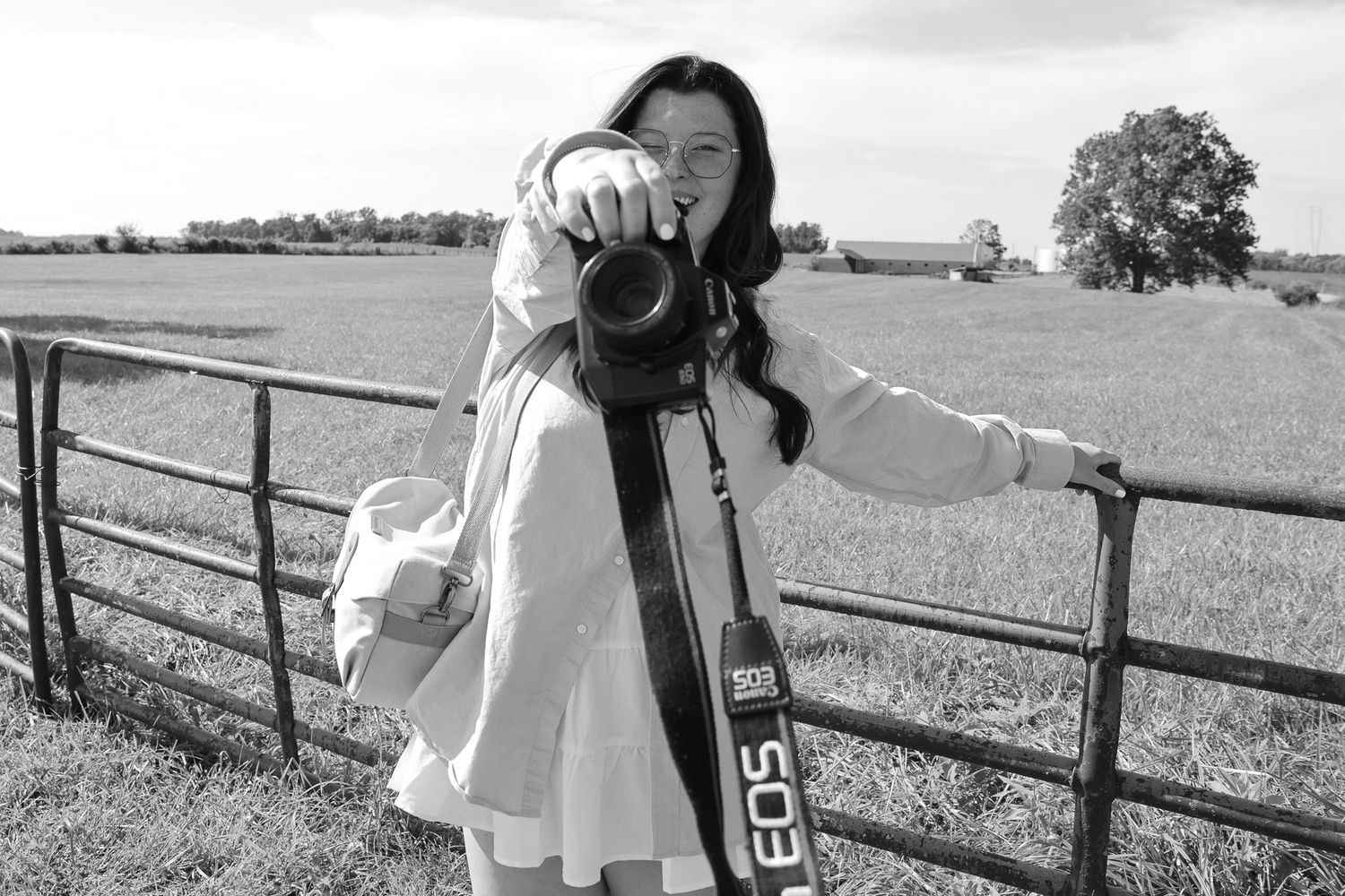 A person in white clothing stands near a wooden fence in a rural setting.
