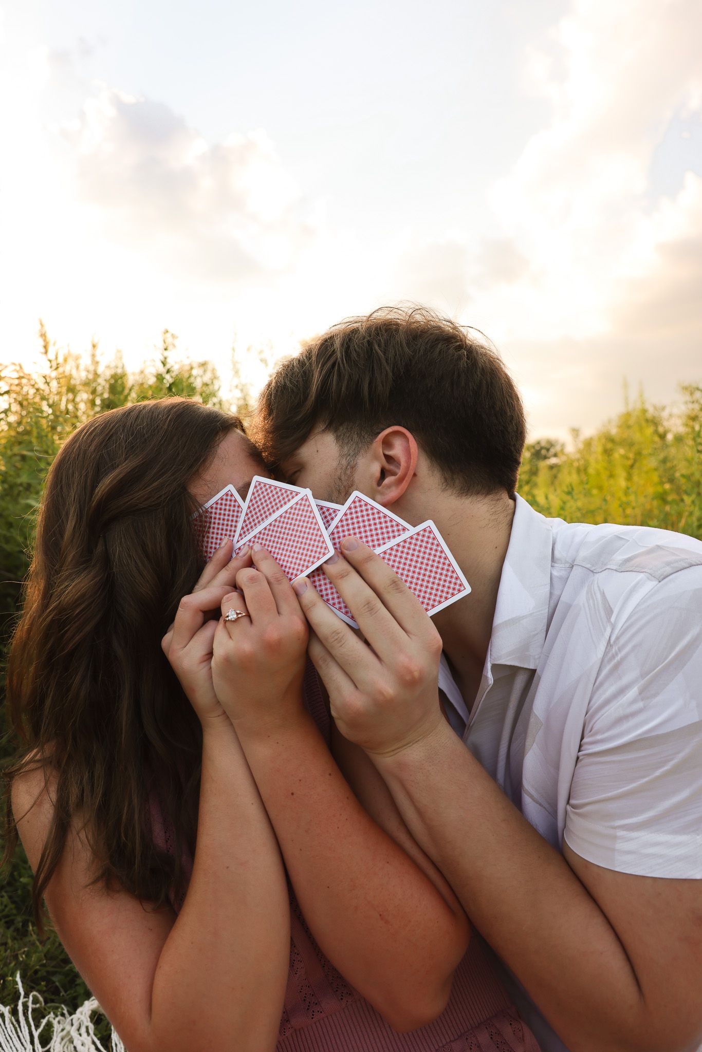 A couple sharing a playful moment behind playing cards in warm evening light.