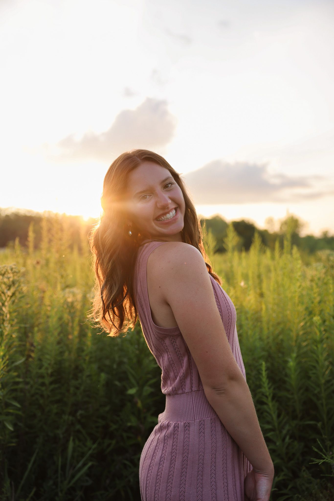 A woman in a purple dress dances joyfully in a sunlit field during golden hour.