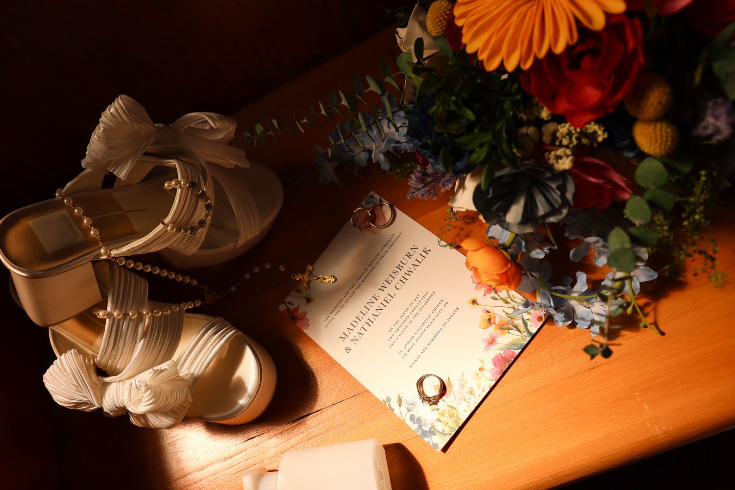 Wedding details including rings, flowers and accessories arranged on a warm-lit wooden surface.