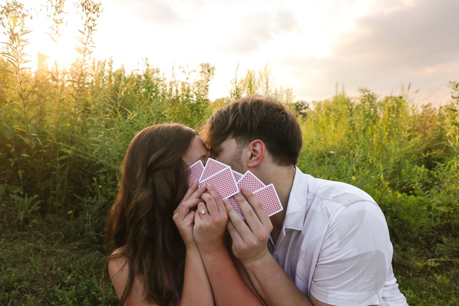 A tender moment between two people concealing their faces with playing cards at sunset.