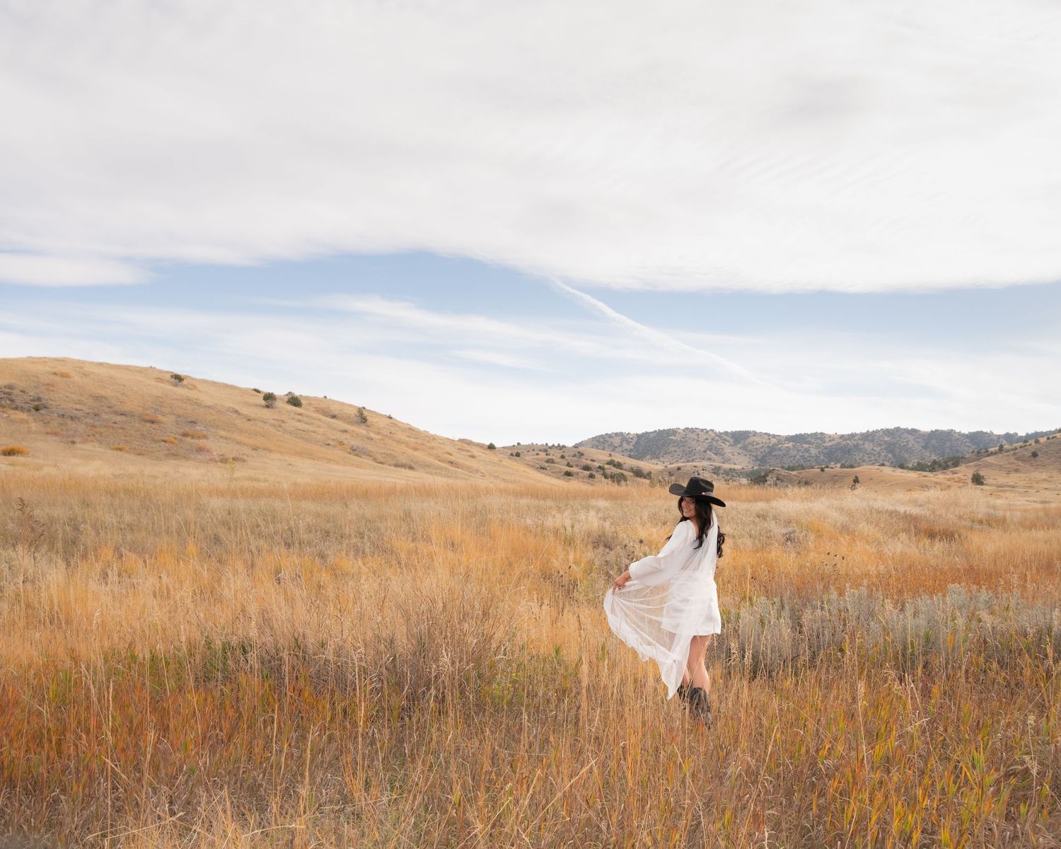 Figure in white dress twirling in golden autumn field with mountains in background.