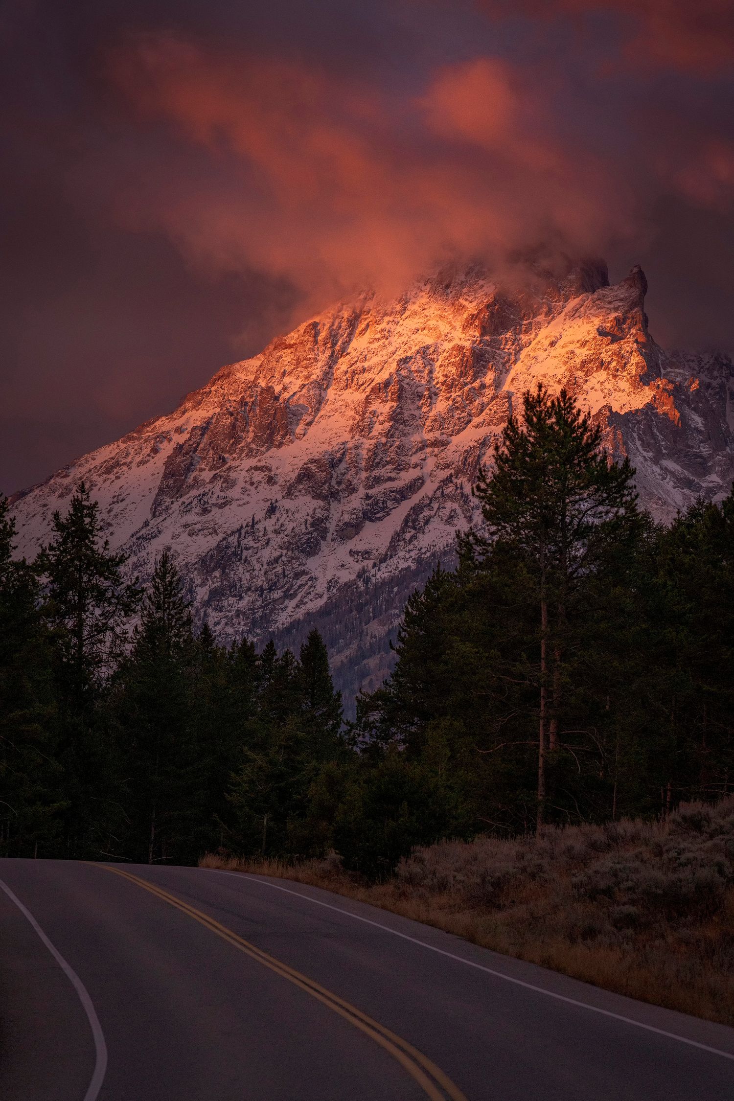 A winding mountain road leads to a dramatically lit peak during sunset in Grand Teton National Park.