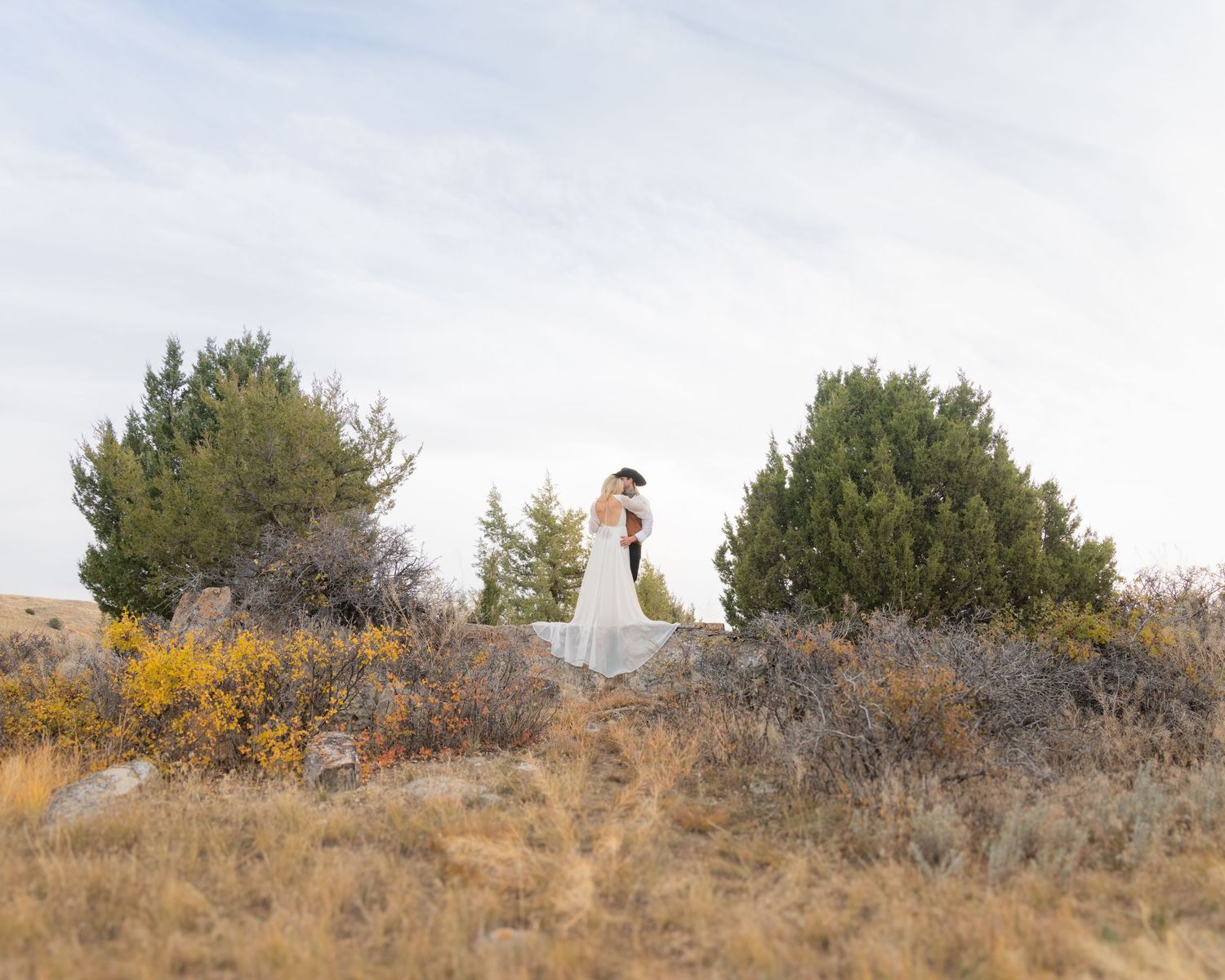 White-dressed figure walking along a hilltop trail with desert brush and autumn colors.