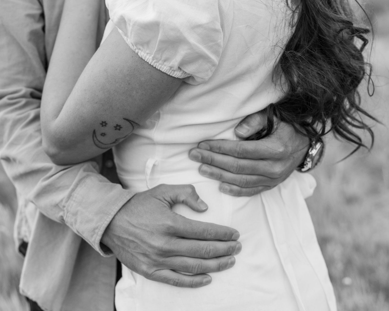 A small smiley face tattoo is visible on someone's arm as they embrace in black and white photography.