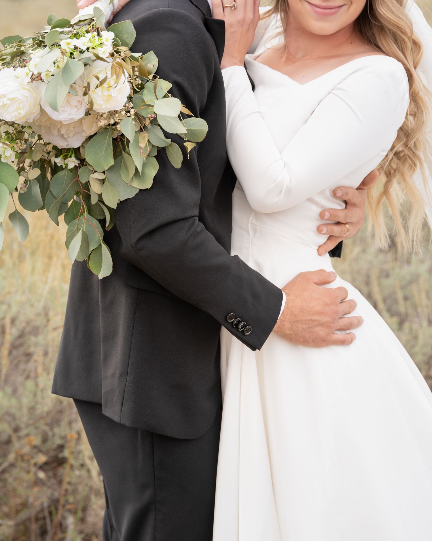 A close-up of wedding attire details featuring a white dress, black suit, and elegant floral bouquet.