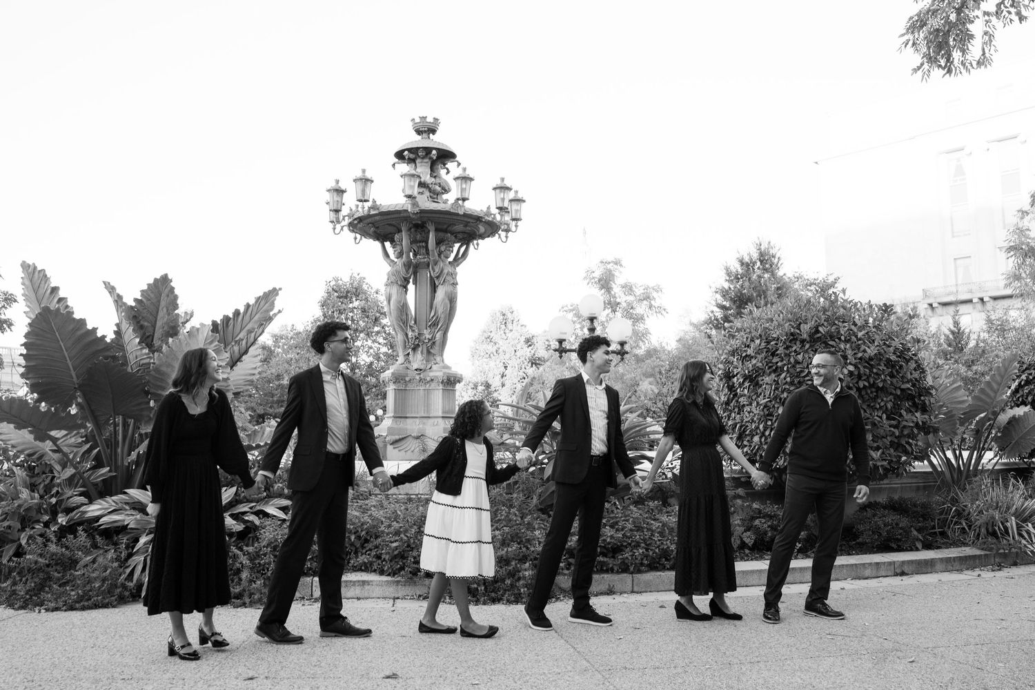 Black and white photograph showing a line of people walking in traditional dress against a rural landscape background.