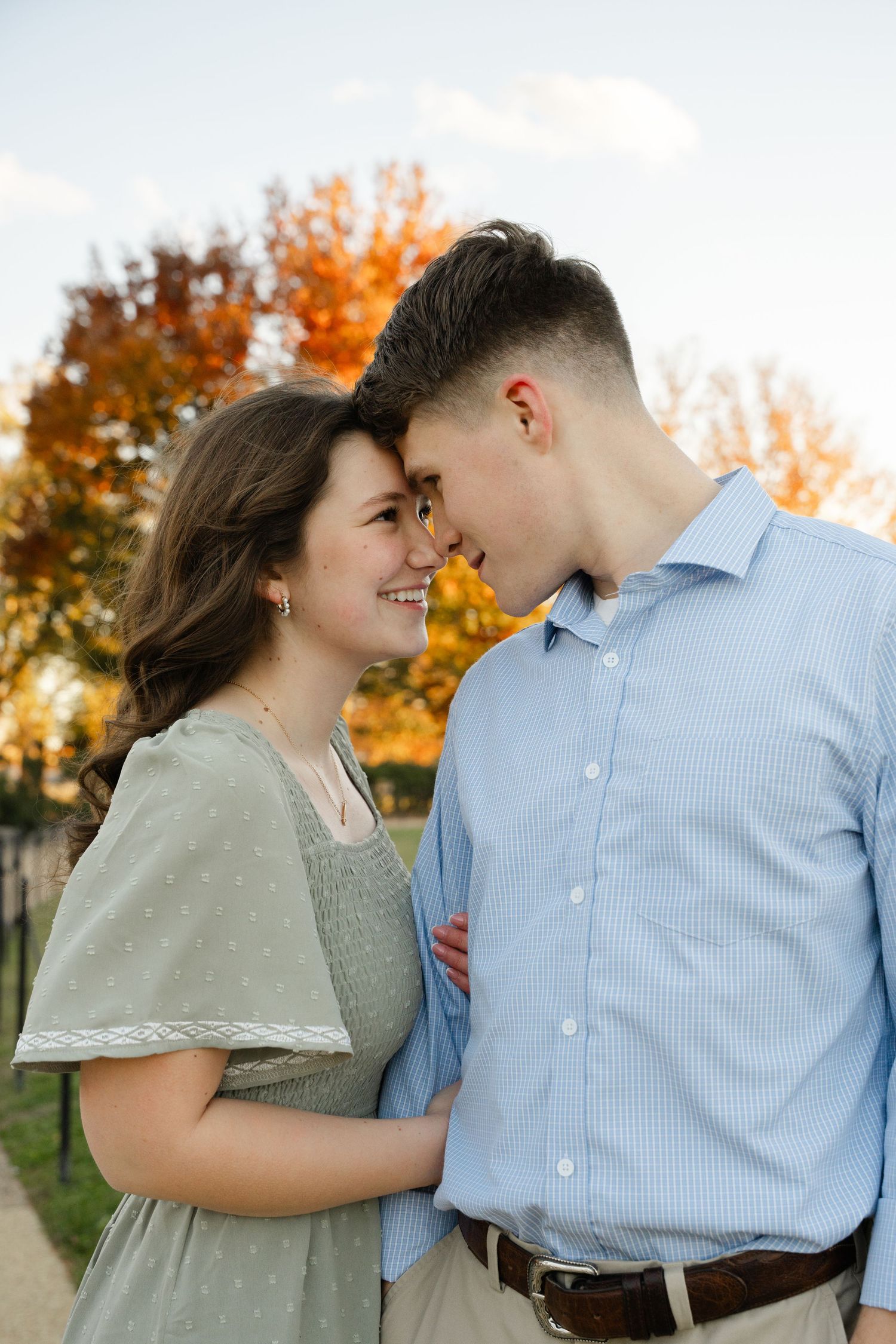 A romantic couple shares an intimate moment outdoors during autumn with colorful fall foliage in the background.