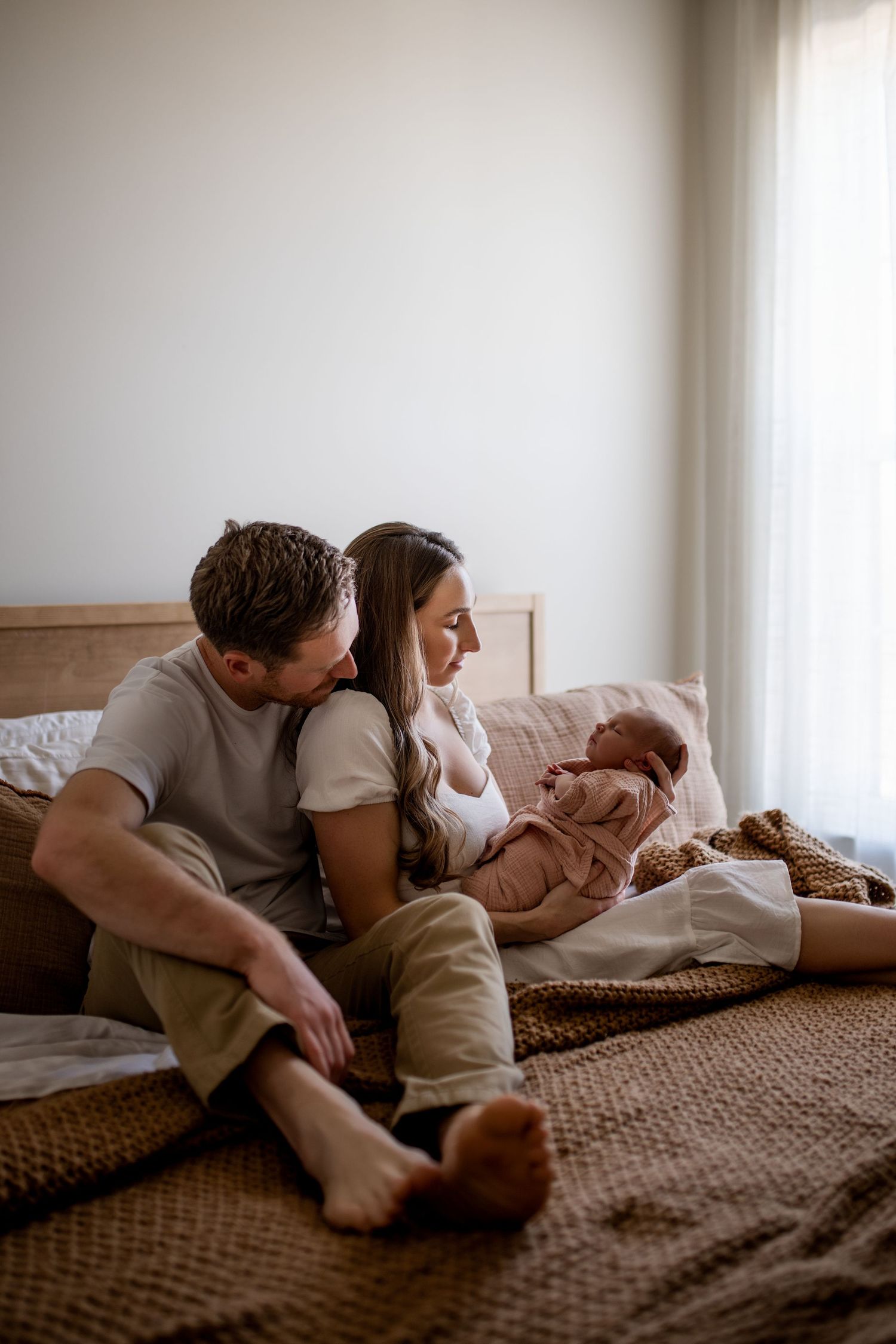 Couple sharing an intimate moment together while relaxing on a brown textured bedspread in natural window light.
