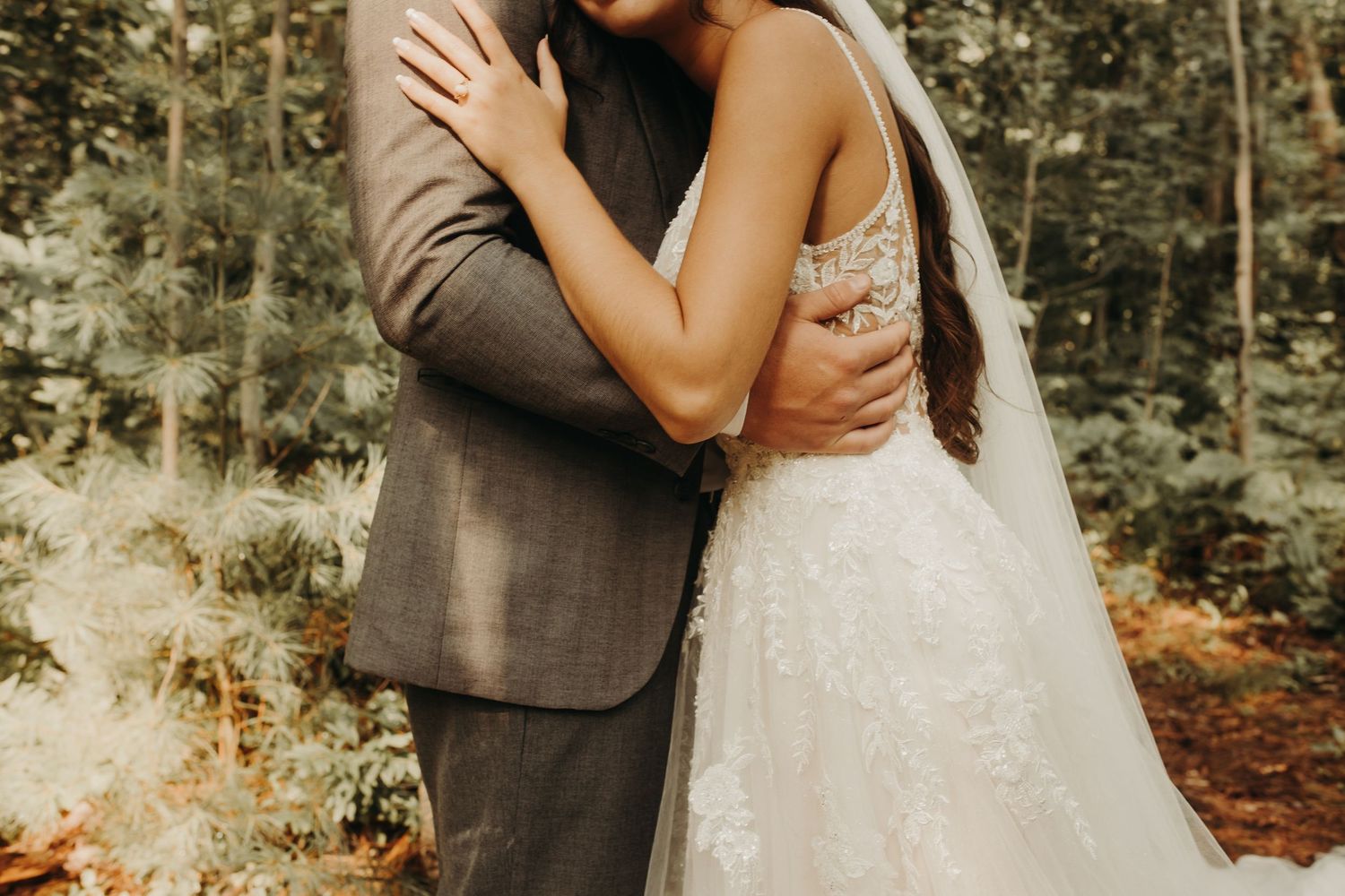 A romantic wedding couple embraces in a sunlit forest setting during their outdoor ceremony.
