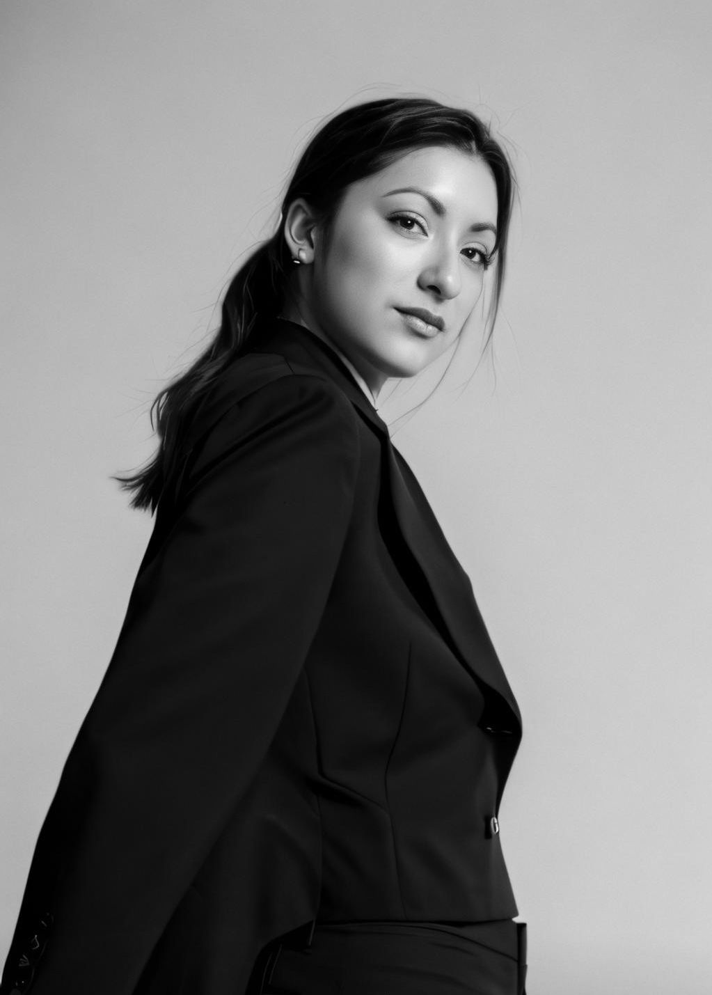 Professional black and white portrait of a model in a black blazer looking over her shoulder.
