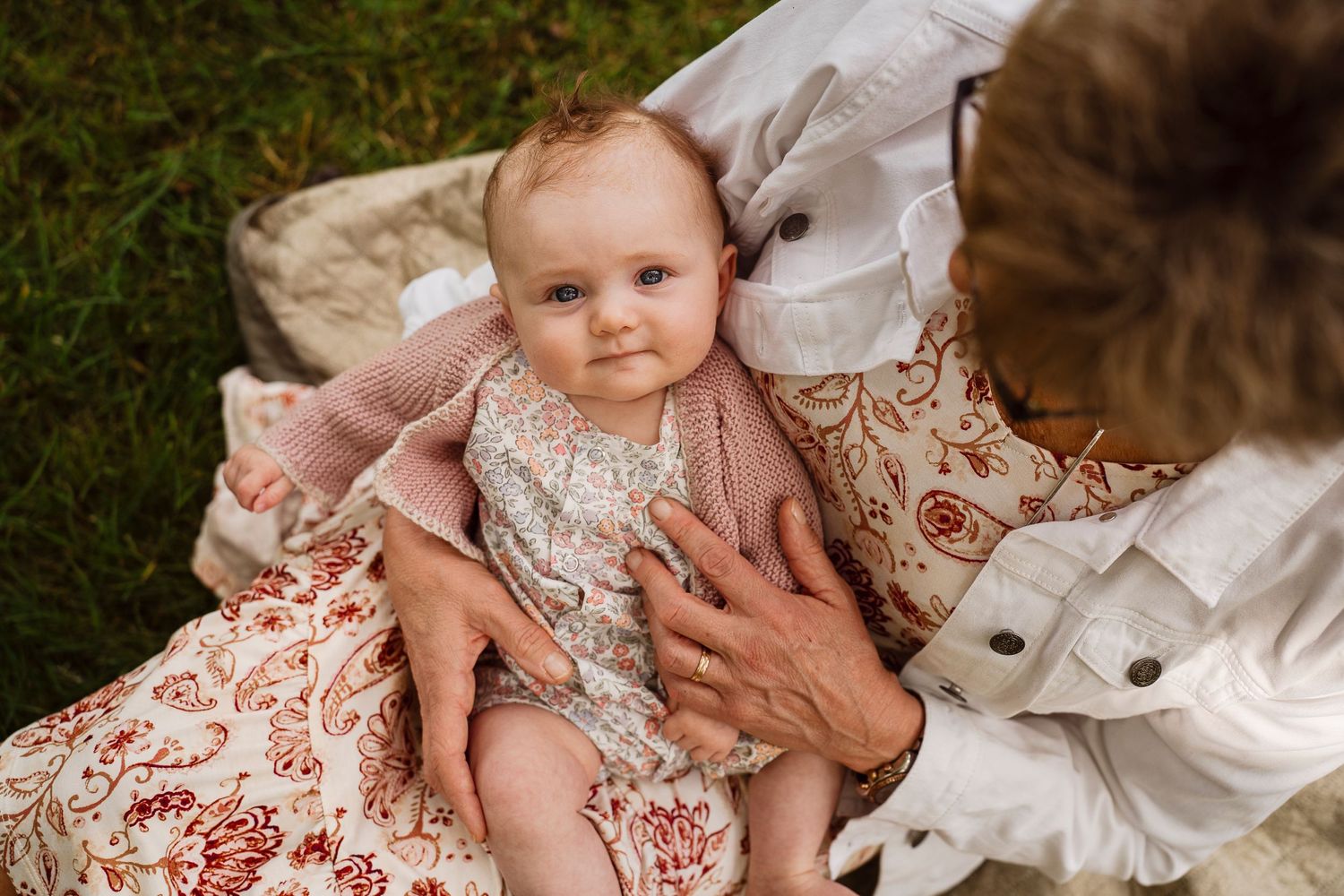Baby wearing lace dress lying on floral blanket outdoors in garden setting.
