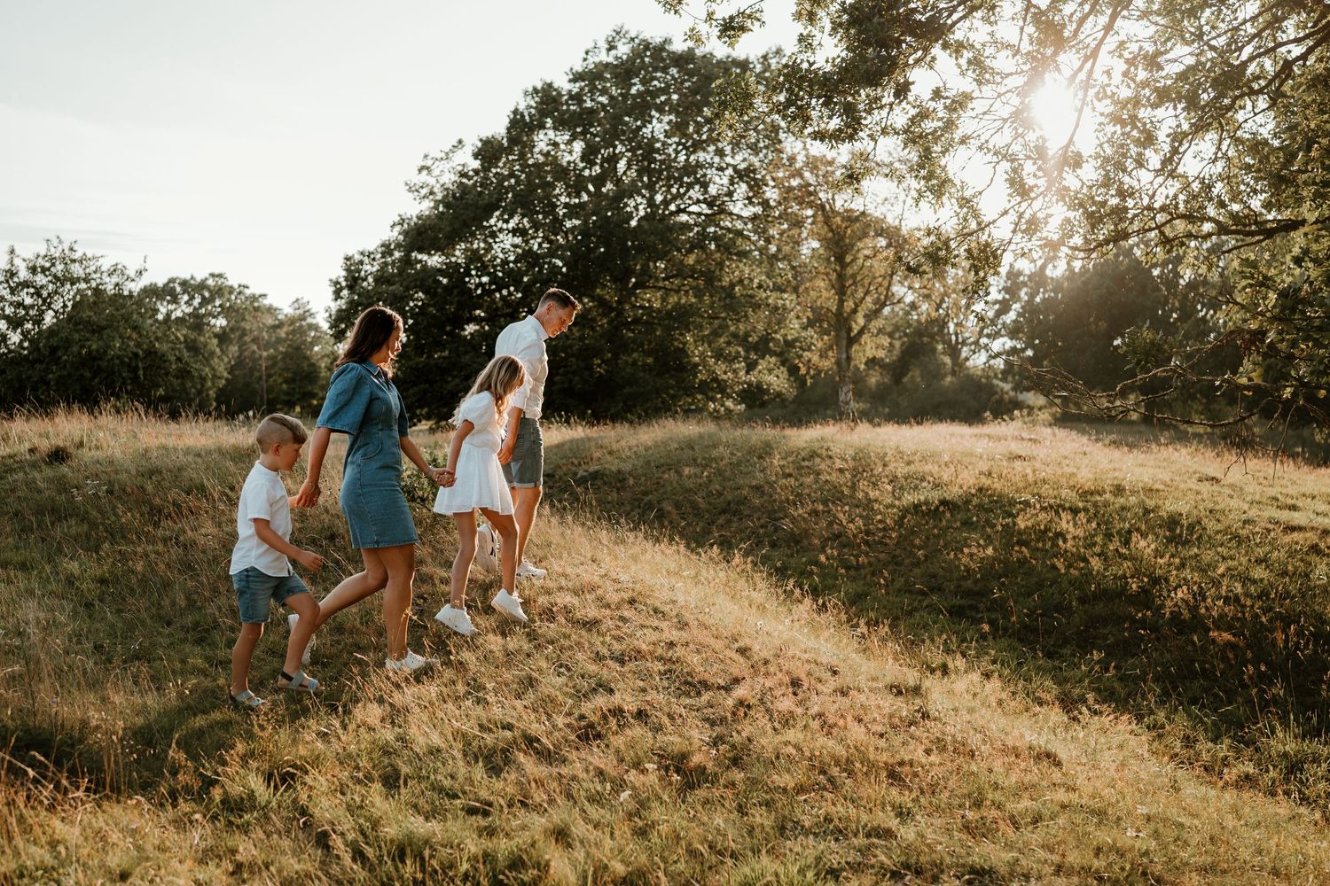 A group walks together up a grassy hillside during golden hour with trees in the background.