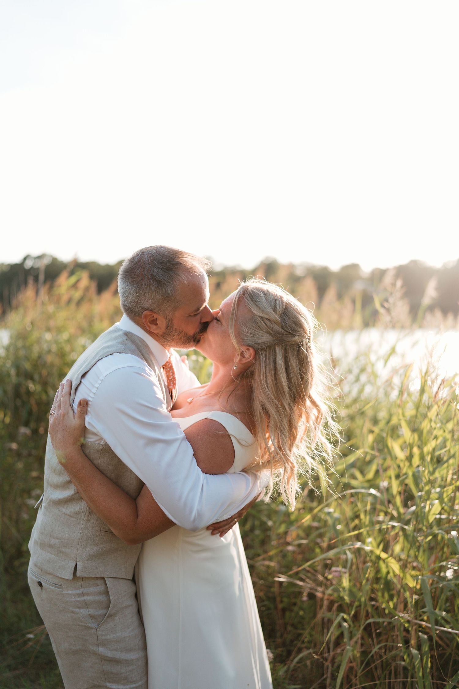 A romantic couple embraces in a sun-lit field of tall grass during golden hour.