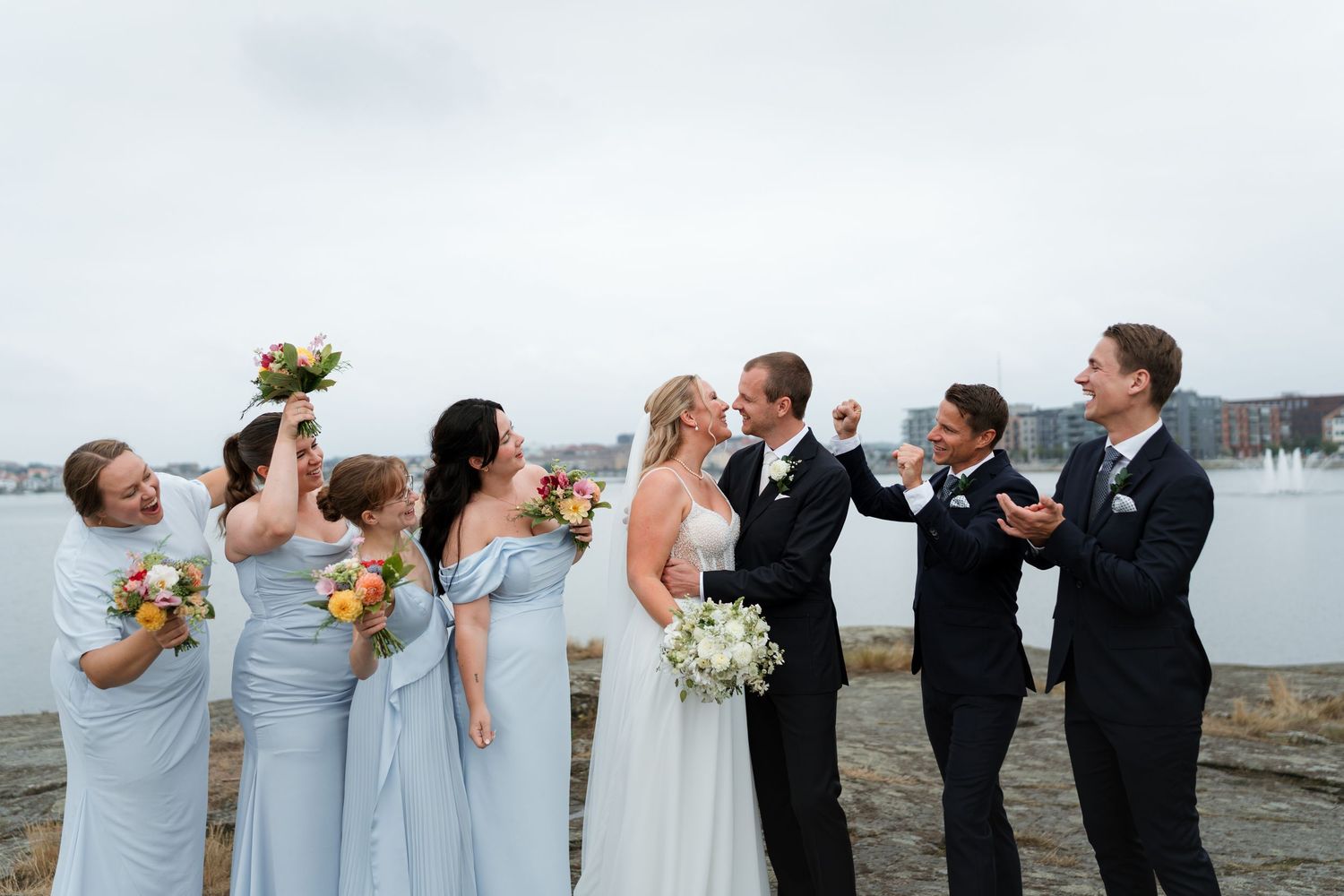 Wedding party in formal attire takes a celebratory drink together on the beach at sunset.
