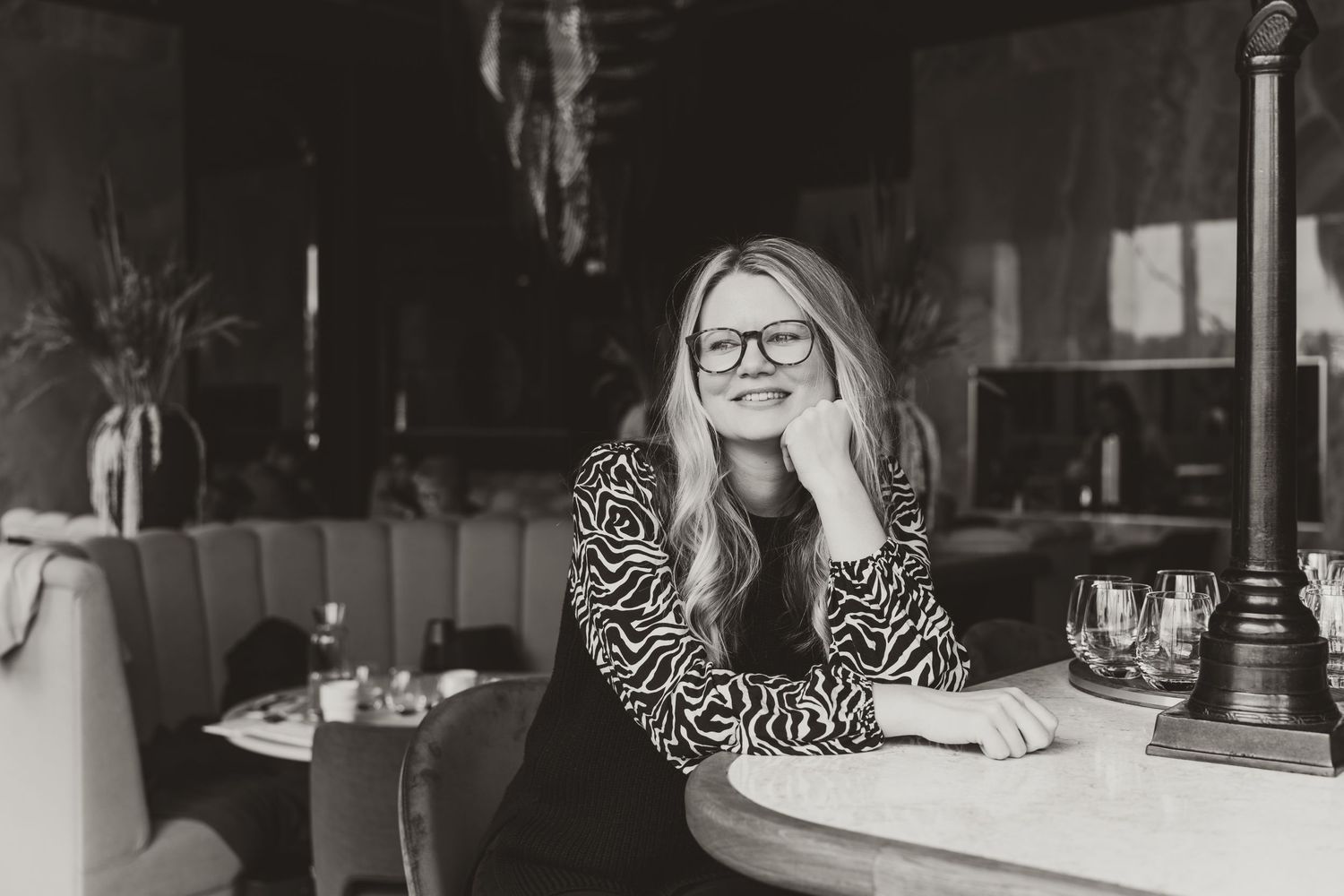 Black and white portrait of person in patterned top smiling at restaurant table.