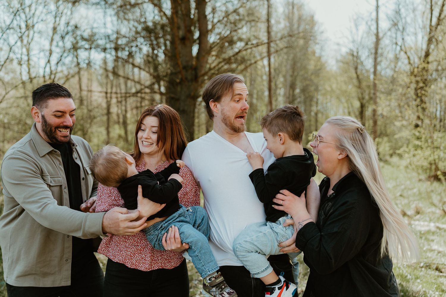 A happy family shares joyful moments together in a wooded outdoor setting during a casual photo session.