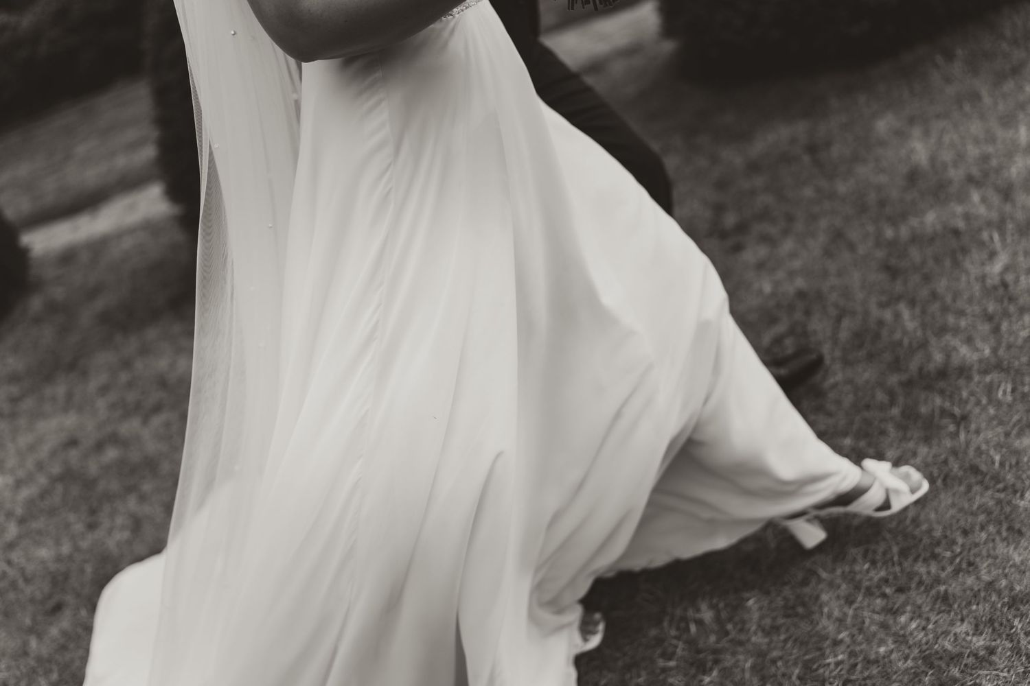 A black and white photograph shows a person in a flowing white dress running through an outdoor garden setting.