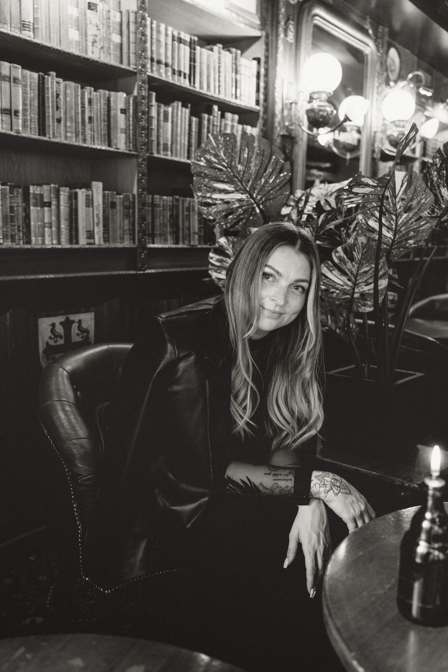 Moody black and white portrait in library setting with bookshelves and candles creating mystical ambiance.
